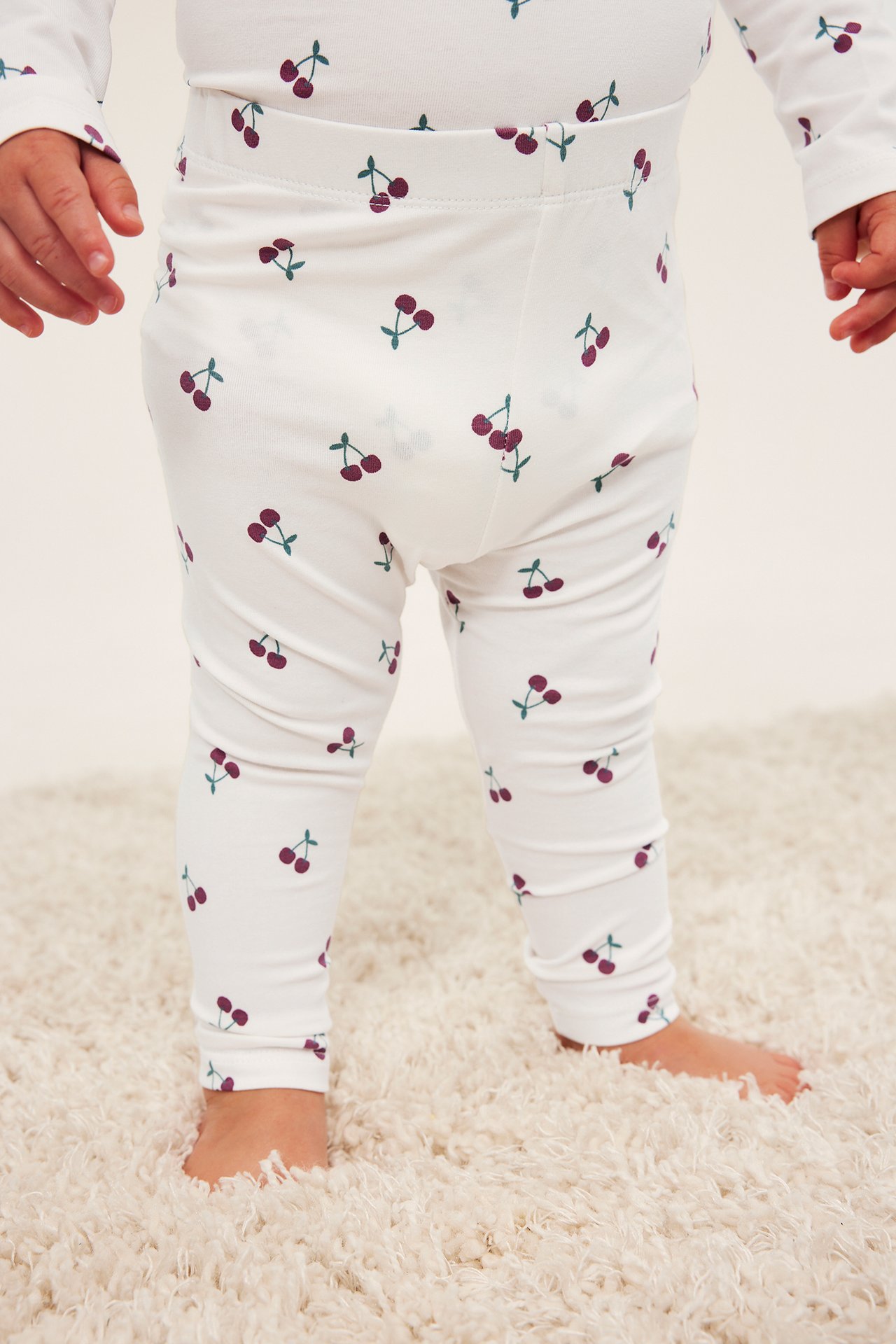 Frontbilde av baby iført hvite kirsebærmønstrede leggings og matchende langermet topp.