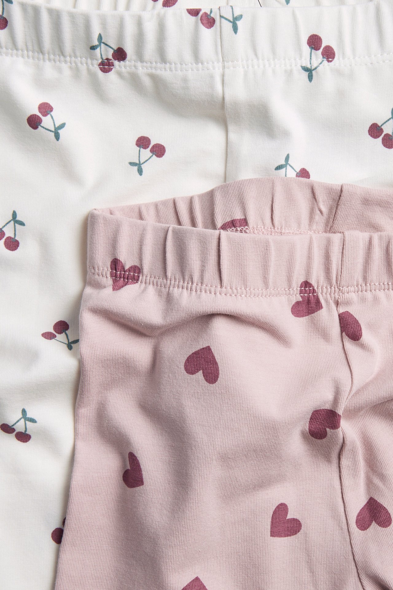 Lähikuva vaaleanpunaisista sydänkuvioisista leggingseistä ja valkoisista kirsikkakuvioisista leggingseistä.