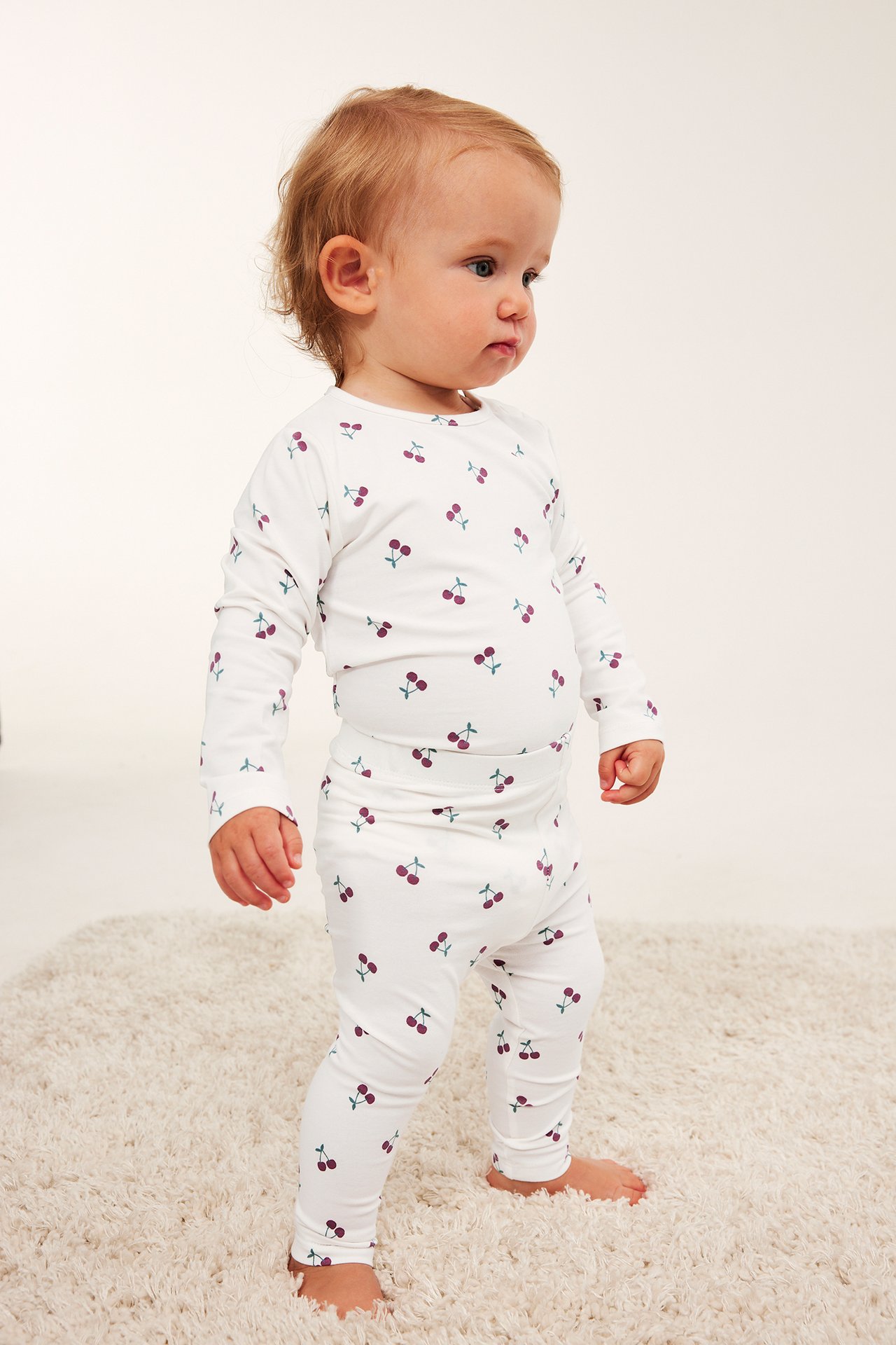 Front-sidevisning av baby i hvit langermet topp og matchende leggings med kirsebærtrykk.