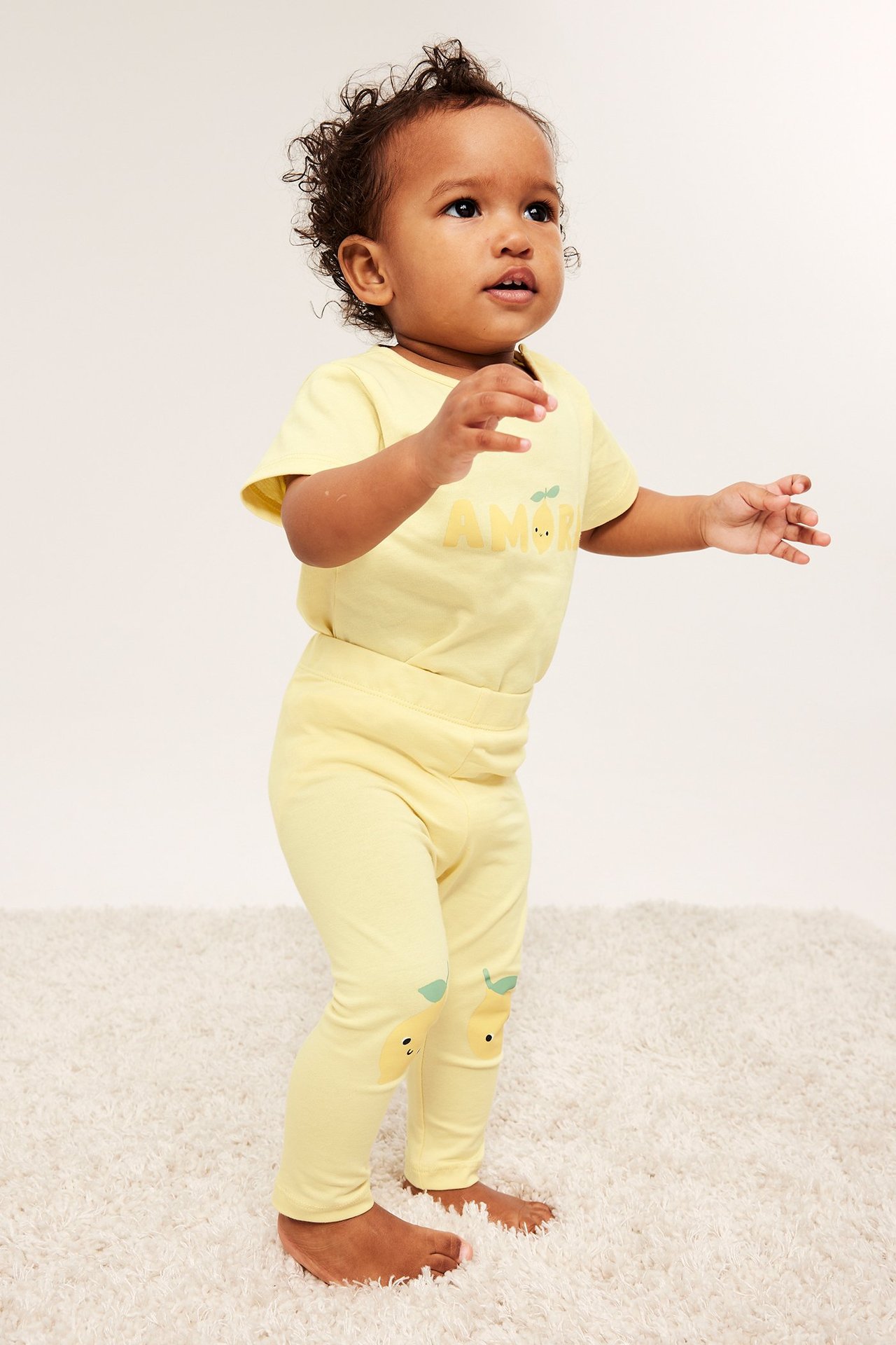 Front view: baby i ljusgul kortärmad bomullsbody med tryck fram, och matchande mönstrade leggings.