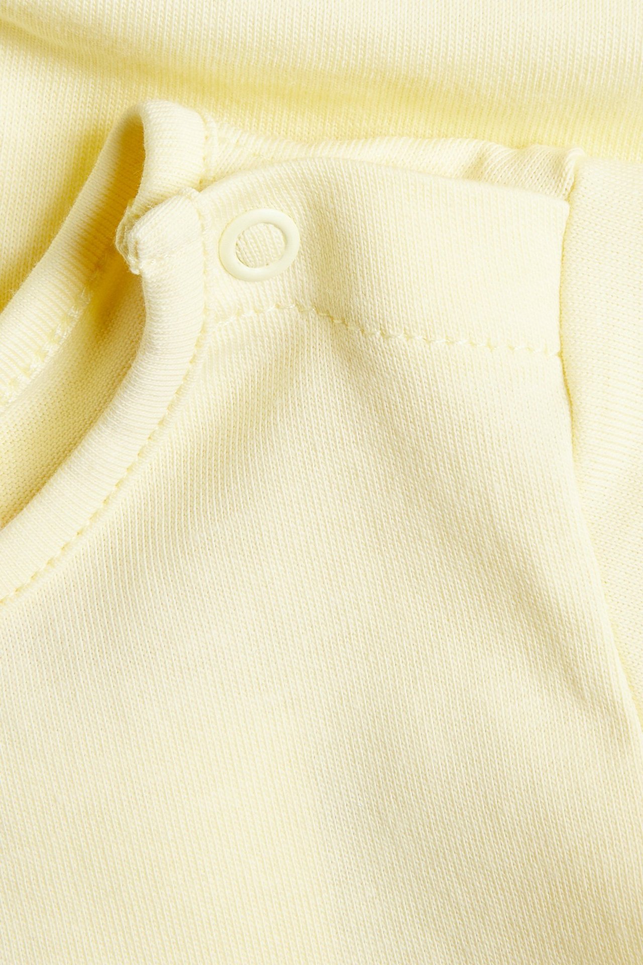 Zbliżenie na jasnożółte, bawełniane body niemowlęce z krótkim rękawem i zatrzaskiem na ramieniu.