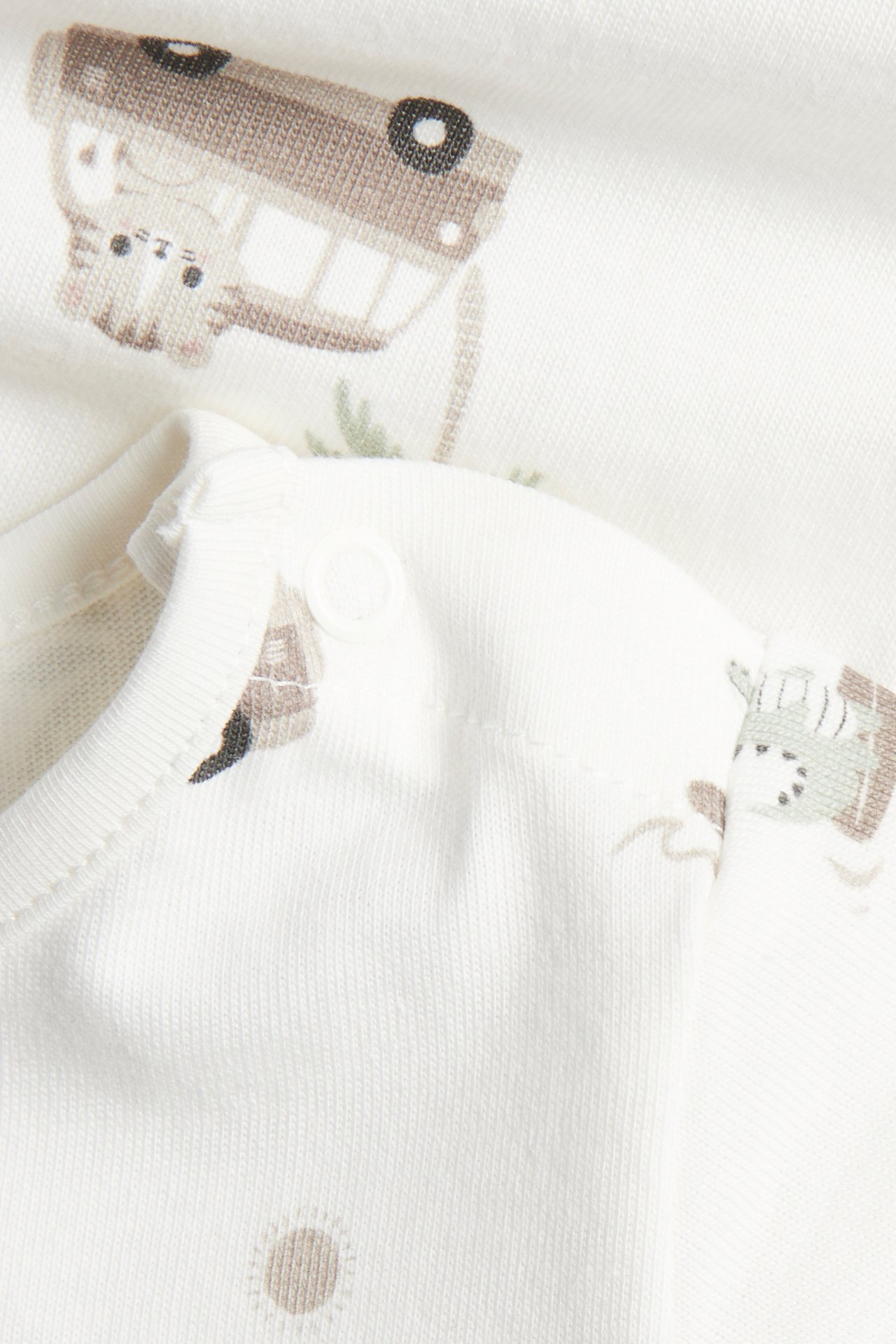 Lähikuva beigestä puuvillaisesta vauvan lyhythihaisesta body-paidasta, jossa on eläin- ja autokuvioita ja olkanapit.