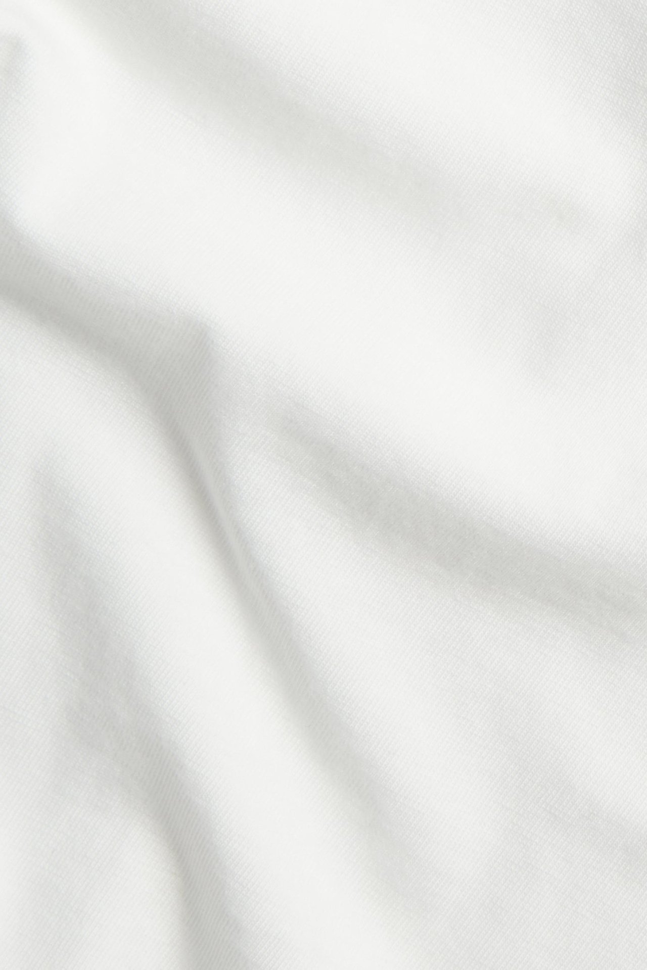Lähikuva luonnonvalkoisesta puuvillasekoite-t-paidan kankaasta pehmeillä laskoksilla ja tekstuurilla.