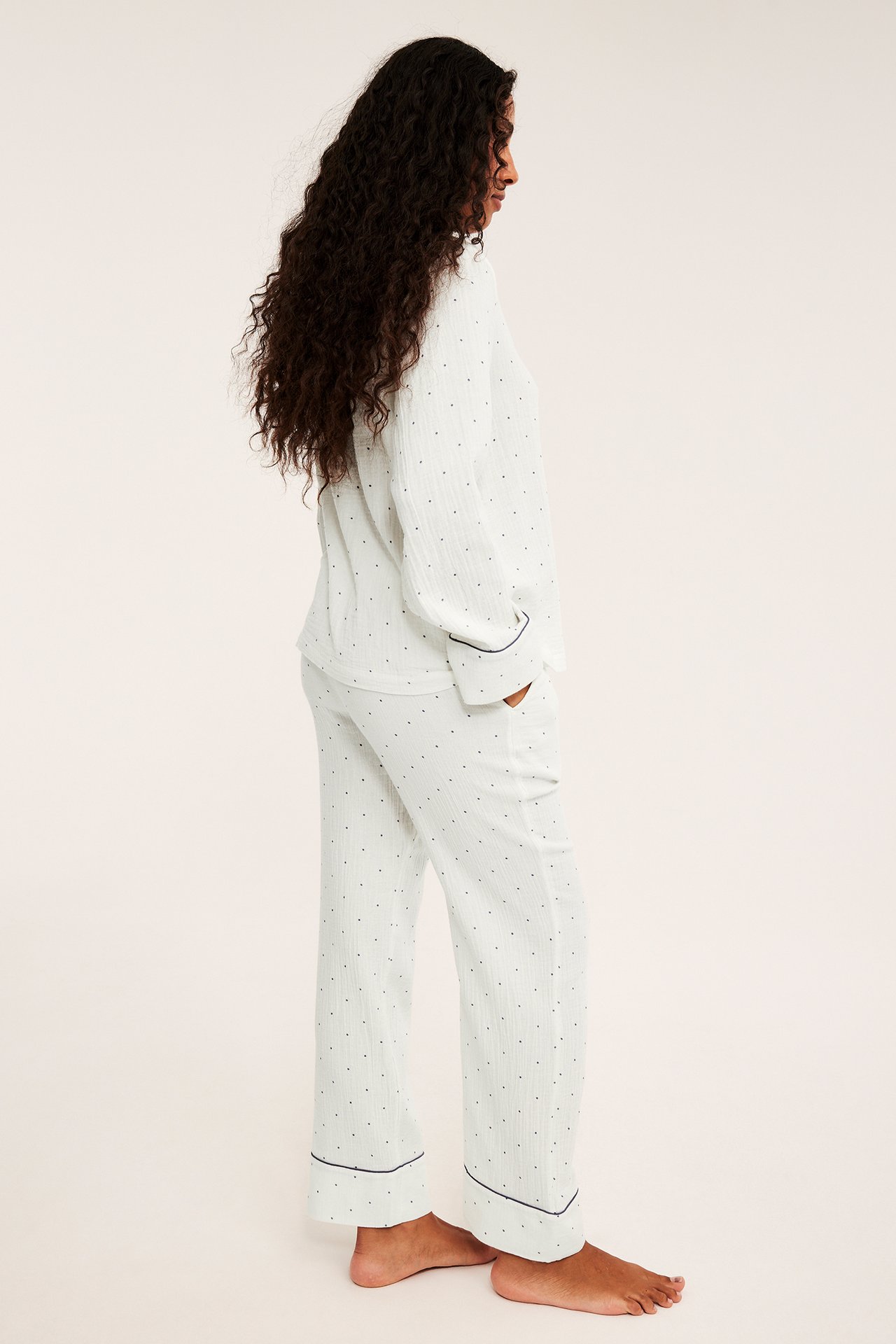 Naisen sivukuva valkoisessa pilkullisessa pyjamassa tummilla tereillä.