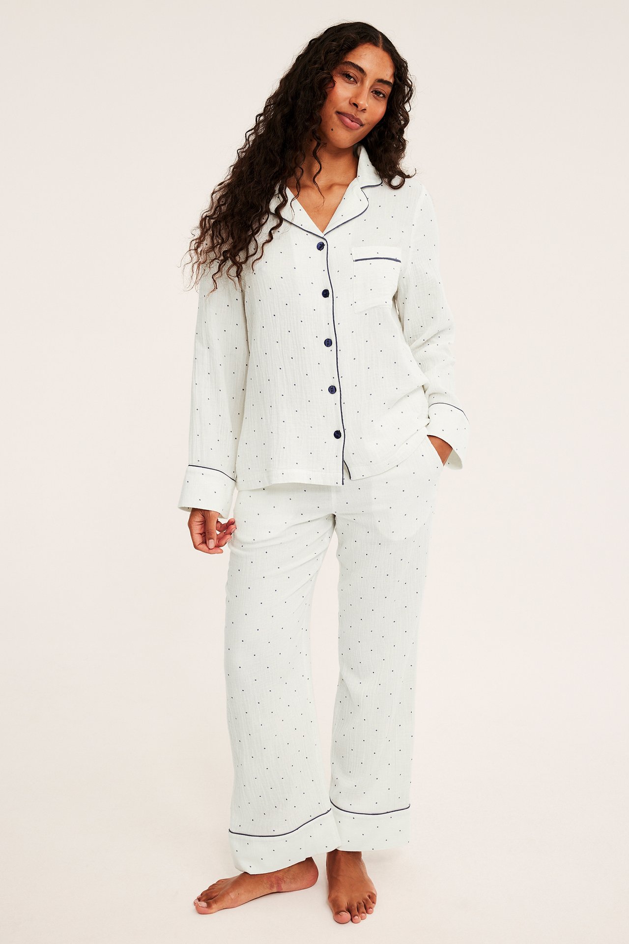 Edestä: Nainen valkoisessa pilkullisessa pyjamassa, jossa laivastonsiniset yksityiskohdat.