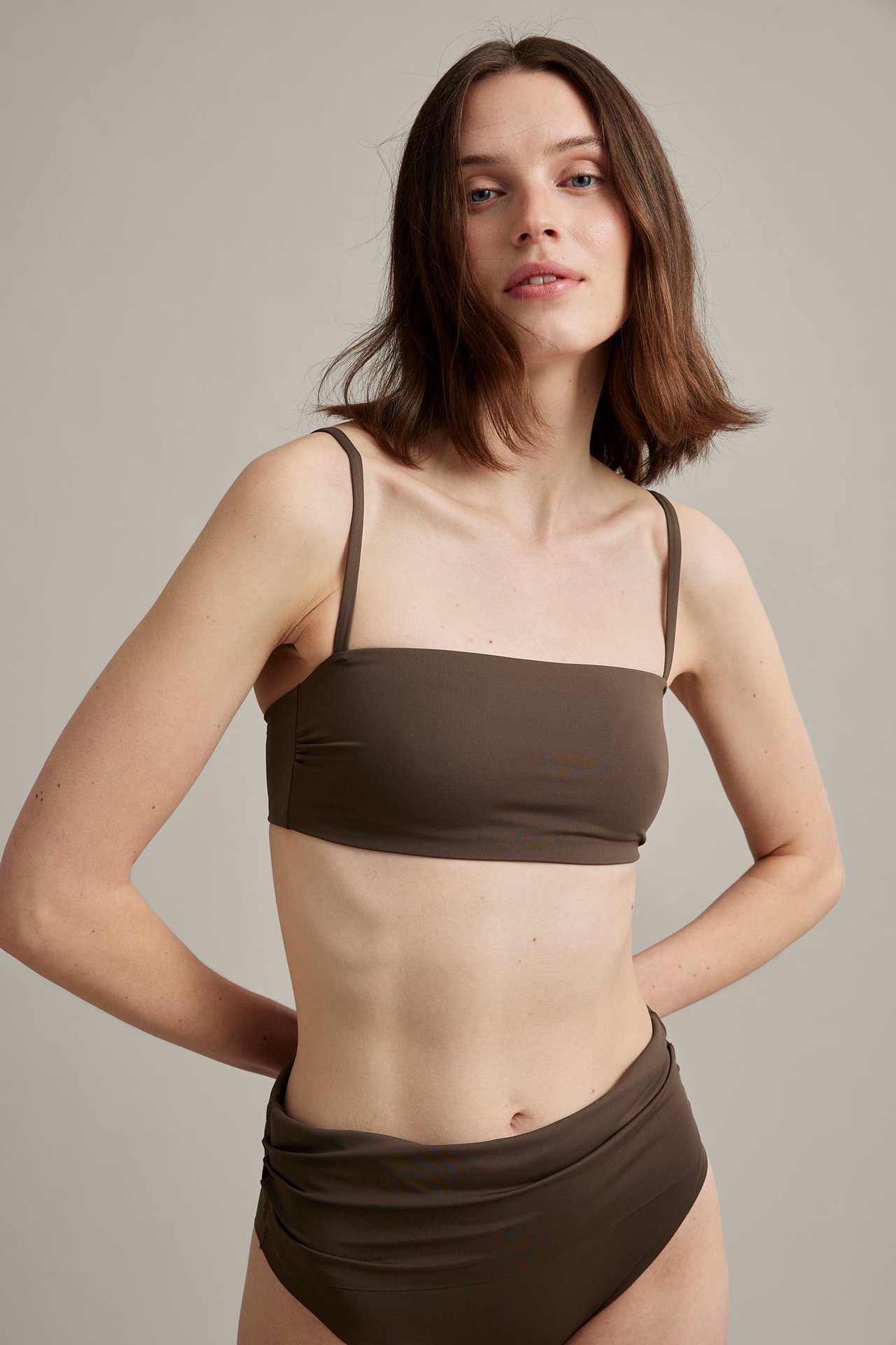 Frontbilde av en kvinne i mørk brun polstret bandeau-bikinitopp med tynne stropper og matchende truse.