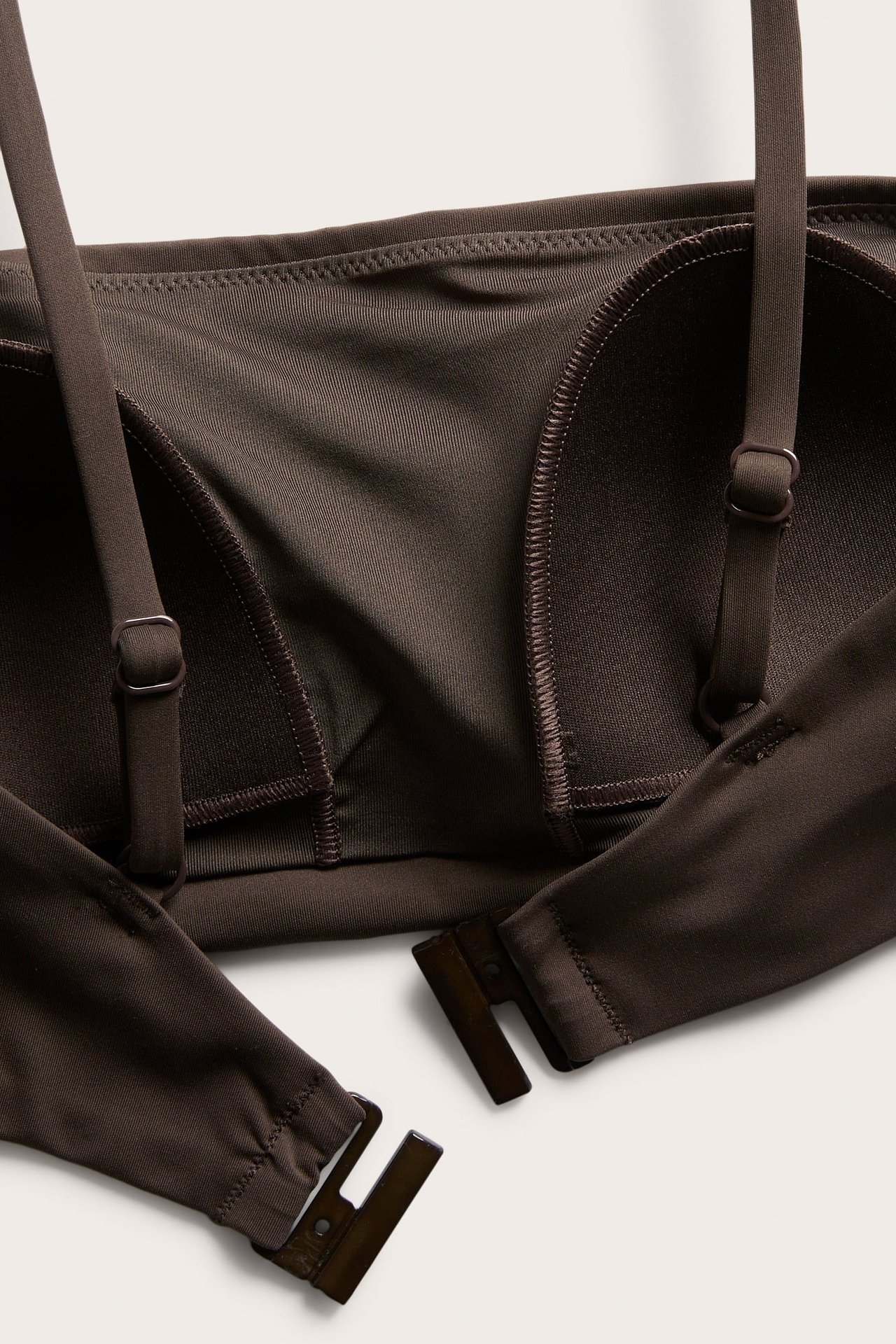 Nærbilde, ovenfra, av en mørkebrun vattert bandeau-bikinitopp med justerbare stropper og rygglås.