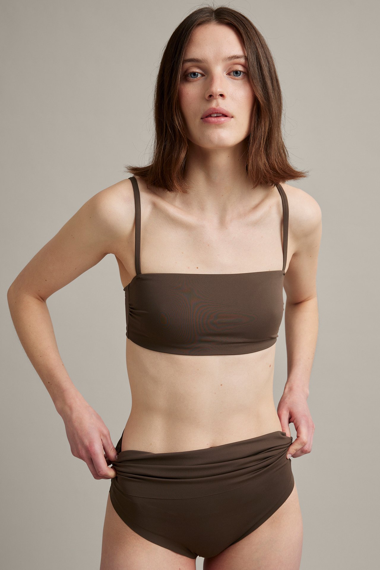 Etunäkymä: nainen tummanruskeissa bikinihousuissa taitettavalla vyötäröllä ja yhteensopivassa bandeau-topissa.