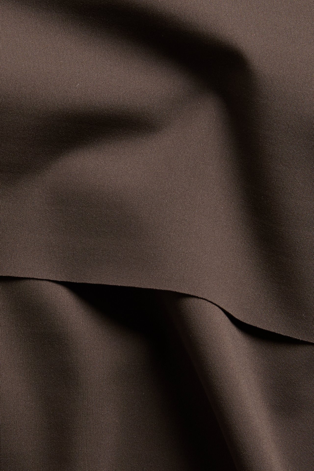 Nærbilde av mørkebrunt bikinitrusestoff med nedbrettbar midje, viser dets glatte textur.