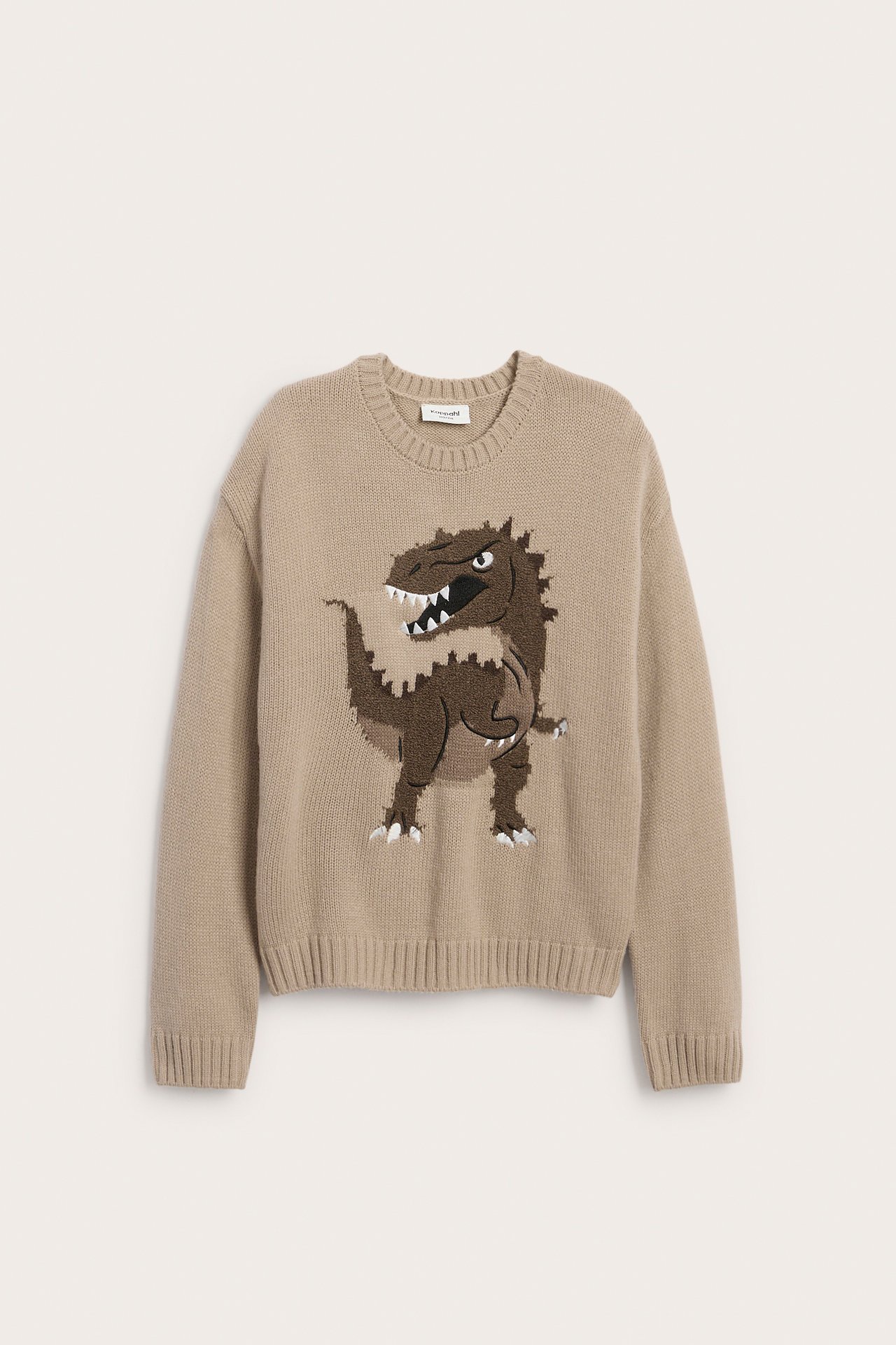 Edestä katsottuna beige neulepusero, jossa ruskea dinosauruskuvio.