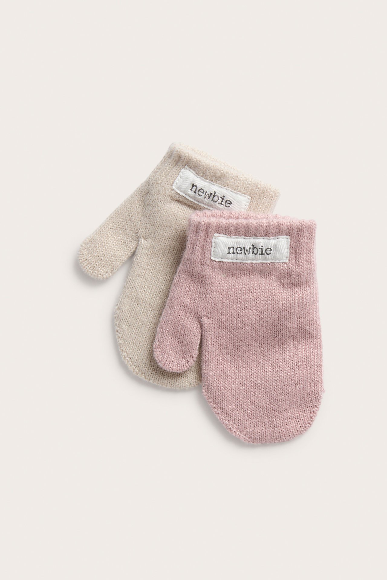 Nærbilde av rosa og beige strikkede babyvotter.