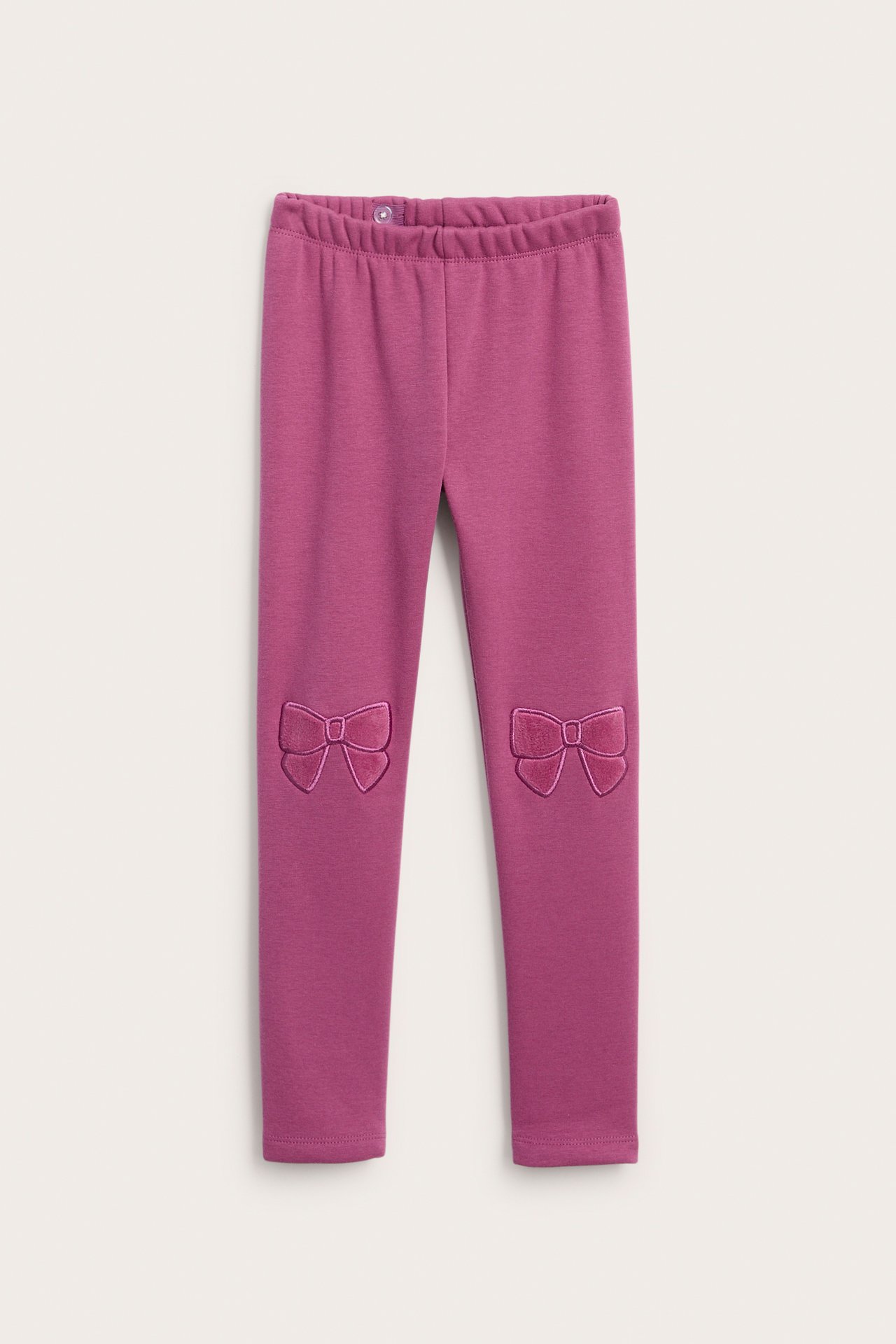 Frontvy av barnleggings i magenta med resår i midjan och broderade rosetter på knäna.