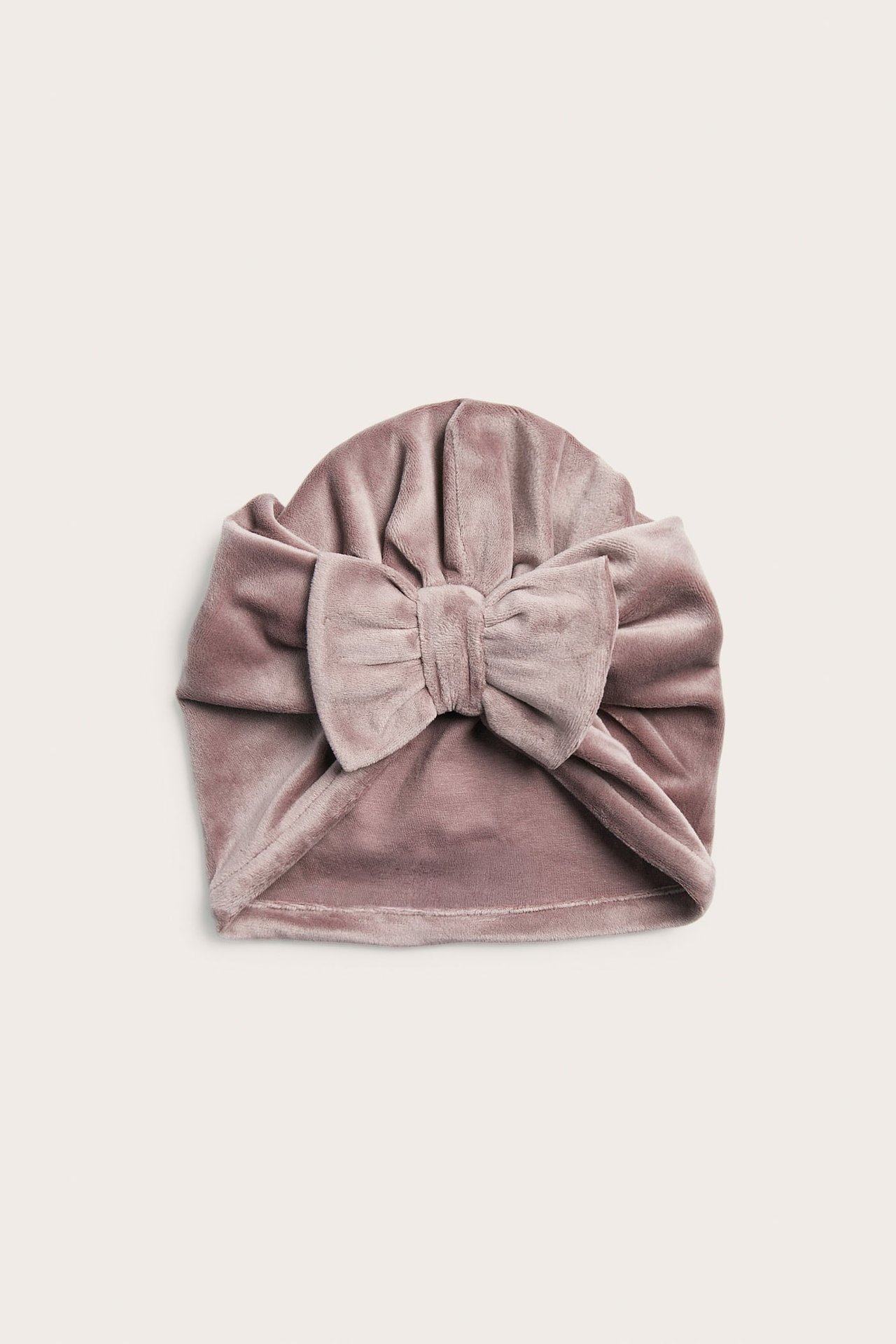 Framifrån, en baby-turban i dammrosa sammet med stor rosett.