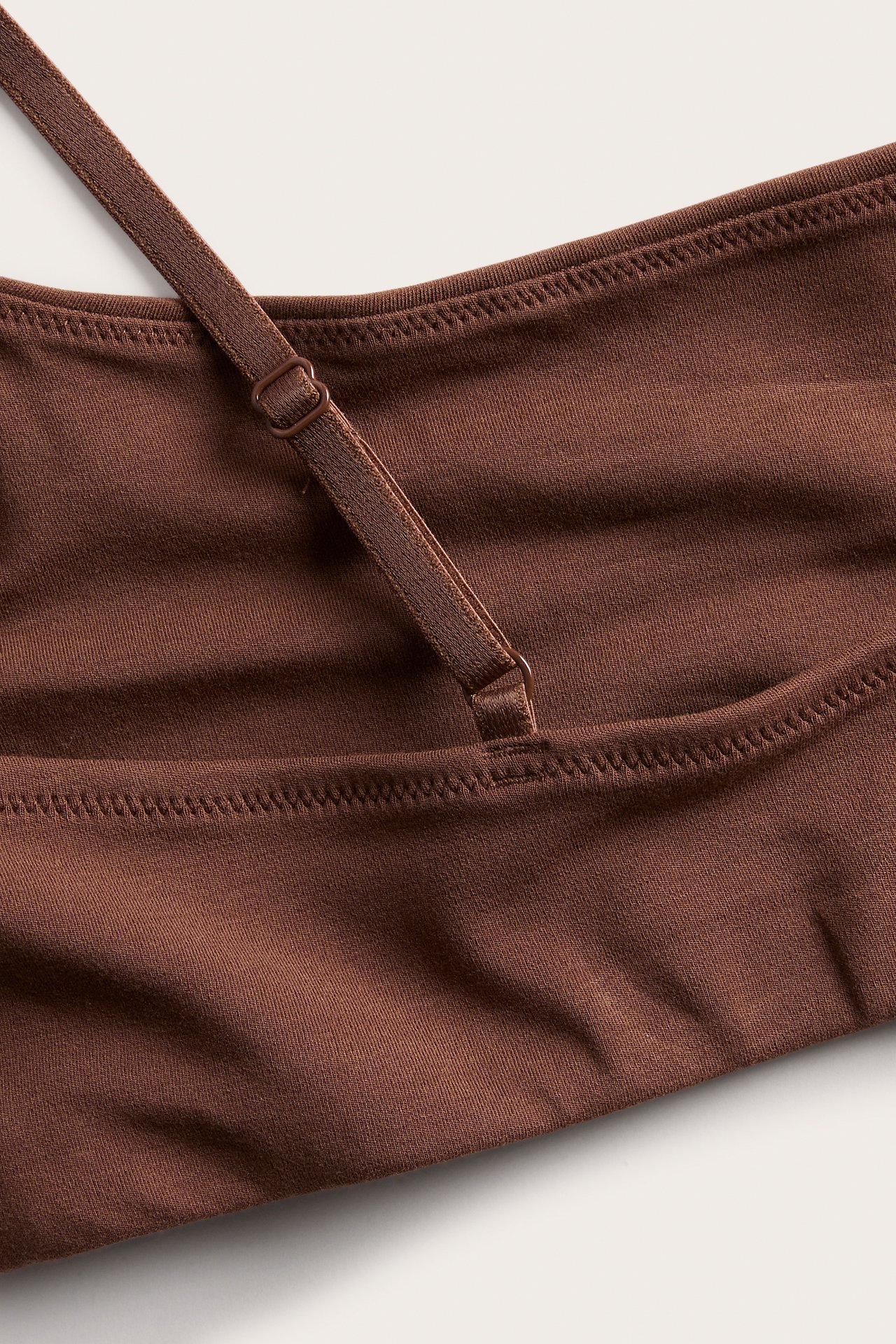 Nærbilde av en brun strikket bralette med justerbar stropp og liten ring.