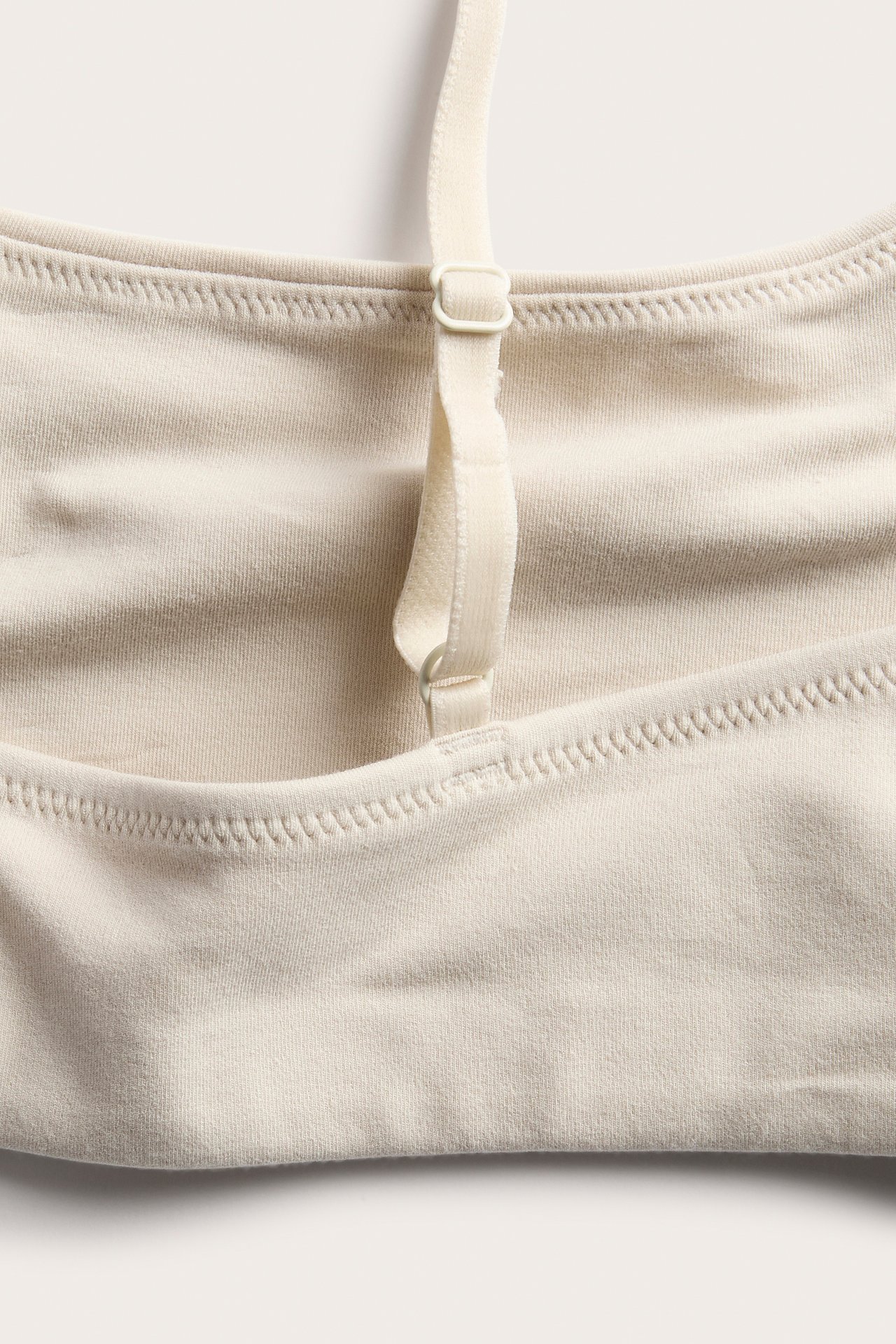 Nærbilde av en lys beige myk strikket bralette med justerbar stropp.