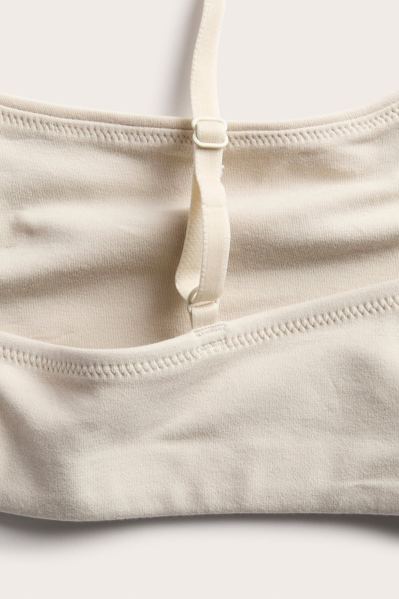 Nærbilde av en lys beige myk strikket bralette med justerbar stropp.