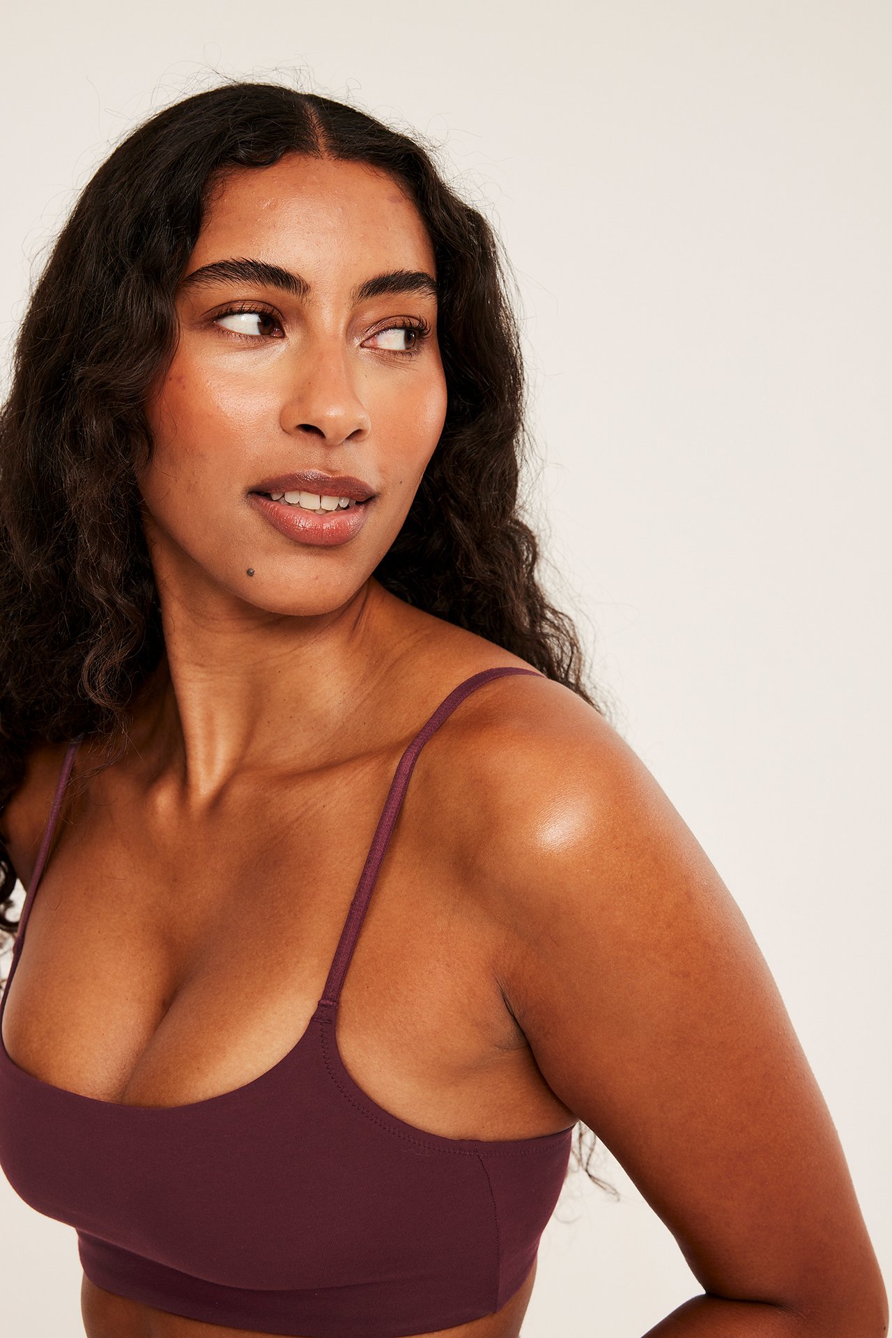 Närbild framifrån på en kvinna i en mörklila bralette.
