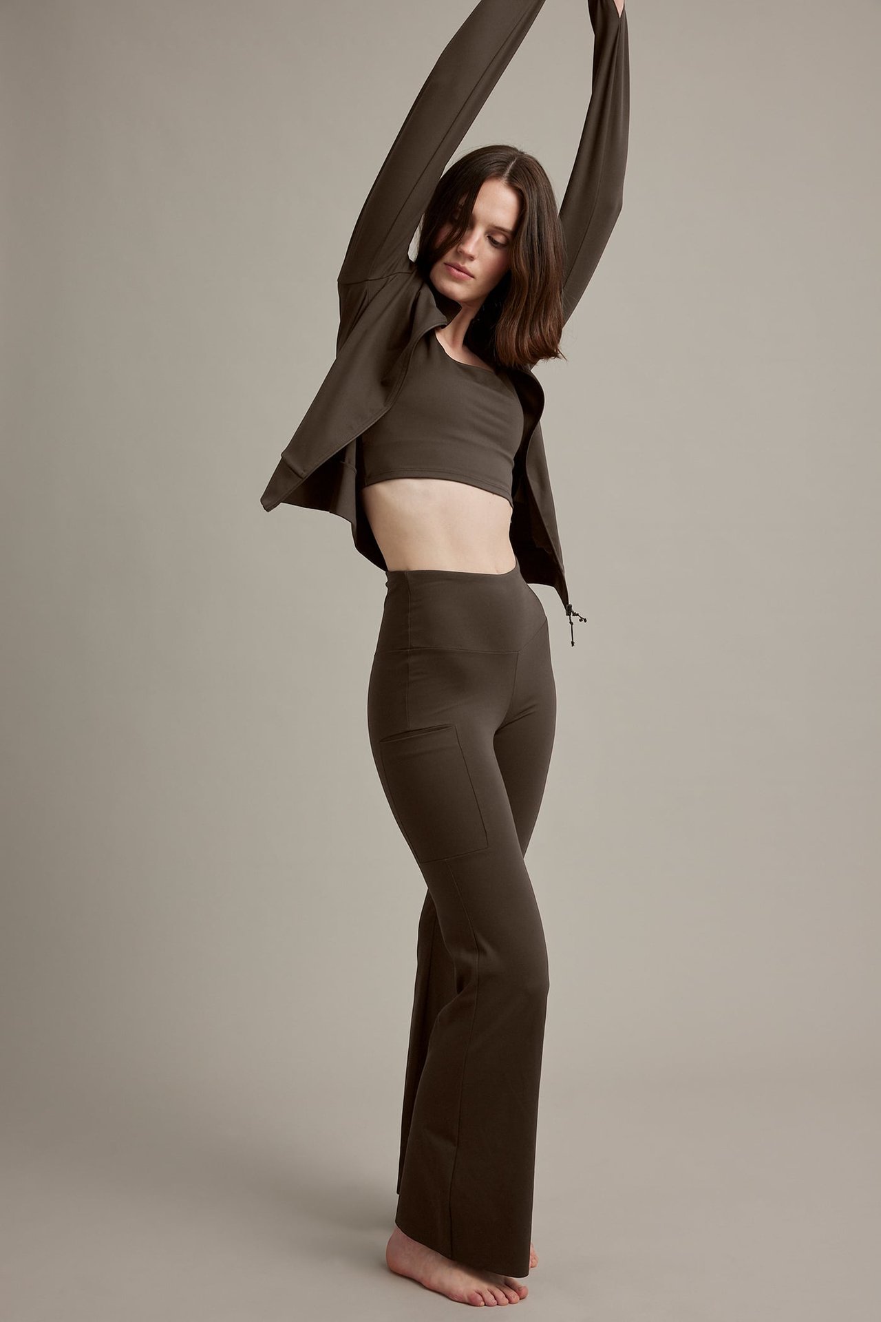 Kvinnlig modell i mörkbruna utsvängda byxor med sidfickor, matchande crop top och öppen jacka.