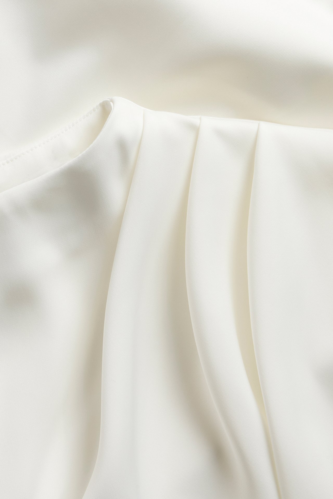 Nærbilde av en offwhite drapert satinbluse, som viser det glatte stoffet og myke folder.