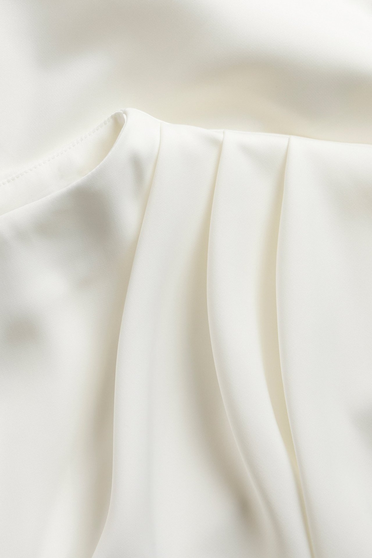 Närbild av en offwhite draperad satinblus, som visar det släta tyget och mjuka vecken.
