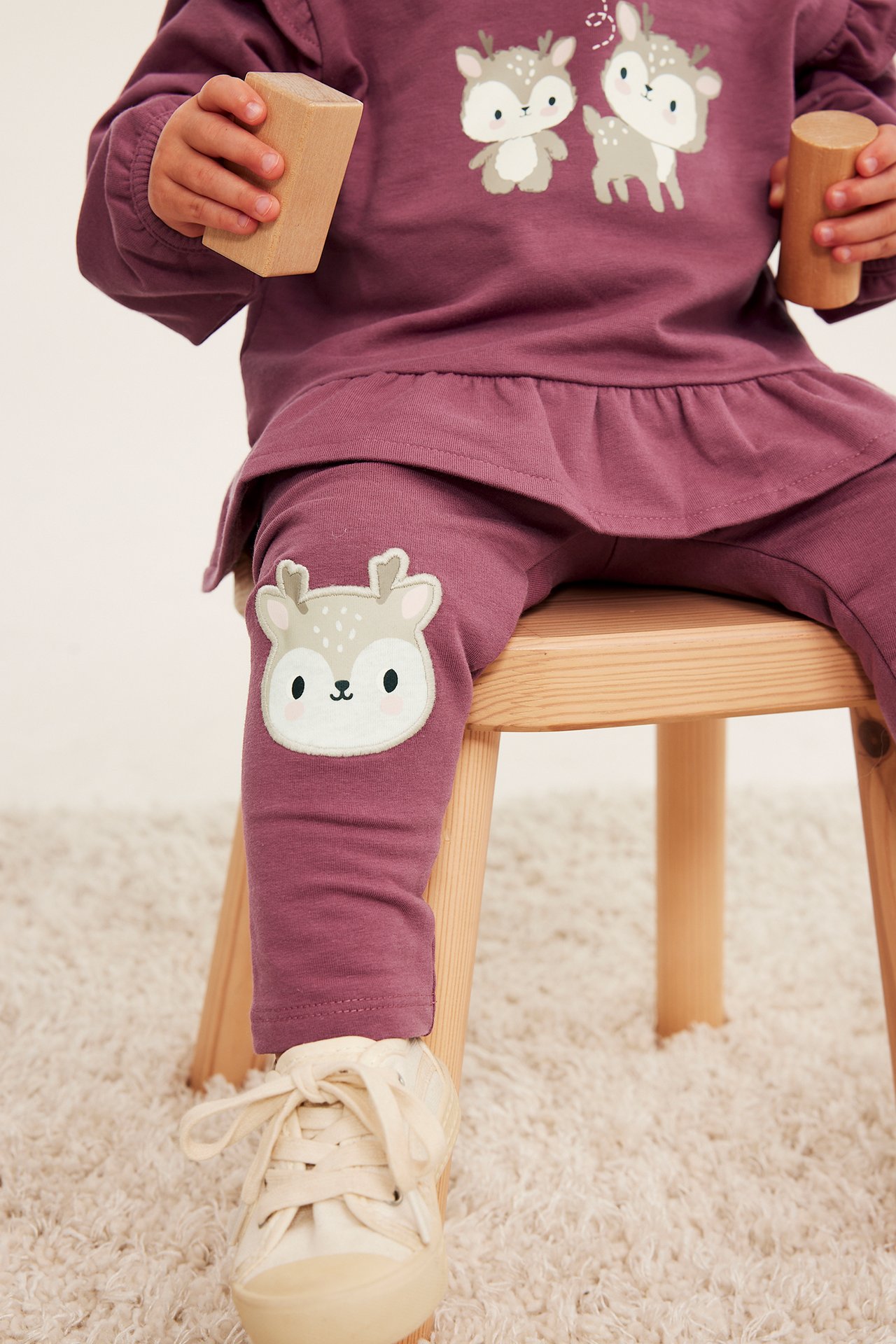 Front: Barn i plommefarget langermet overdel med hjortemotiv og matchende leggings, holder treklosser.