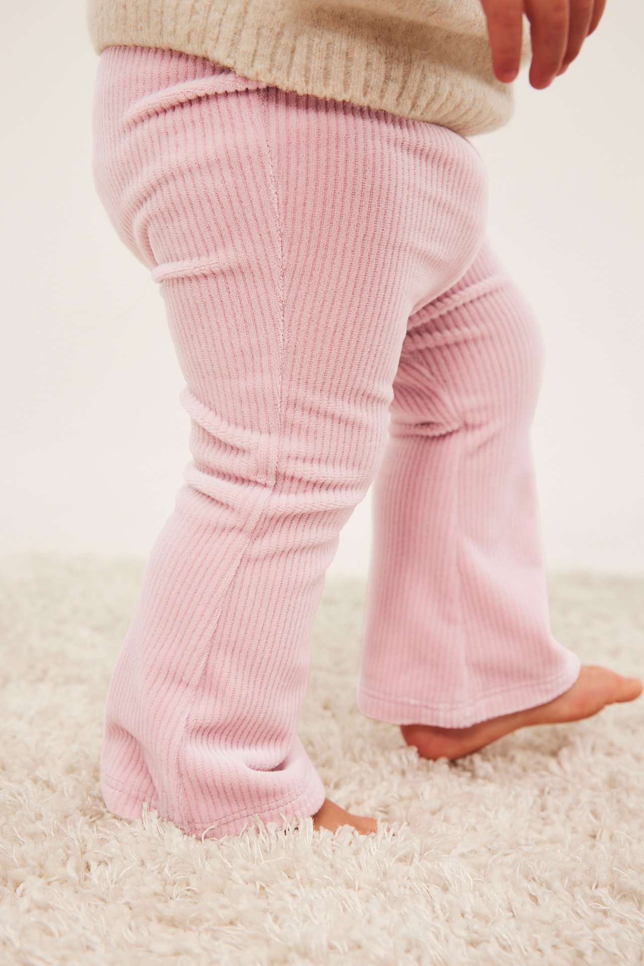 Sidebilde av et barn i rosa kordfløyelsbukser og en beige genser.