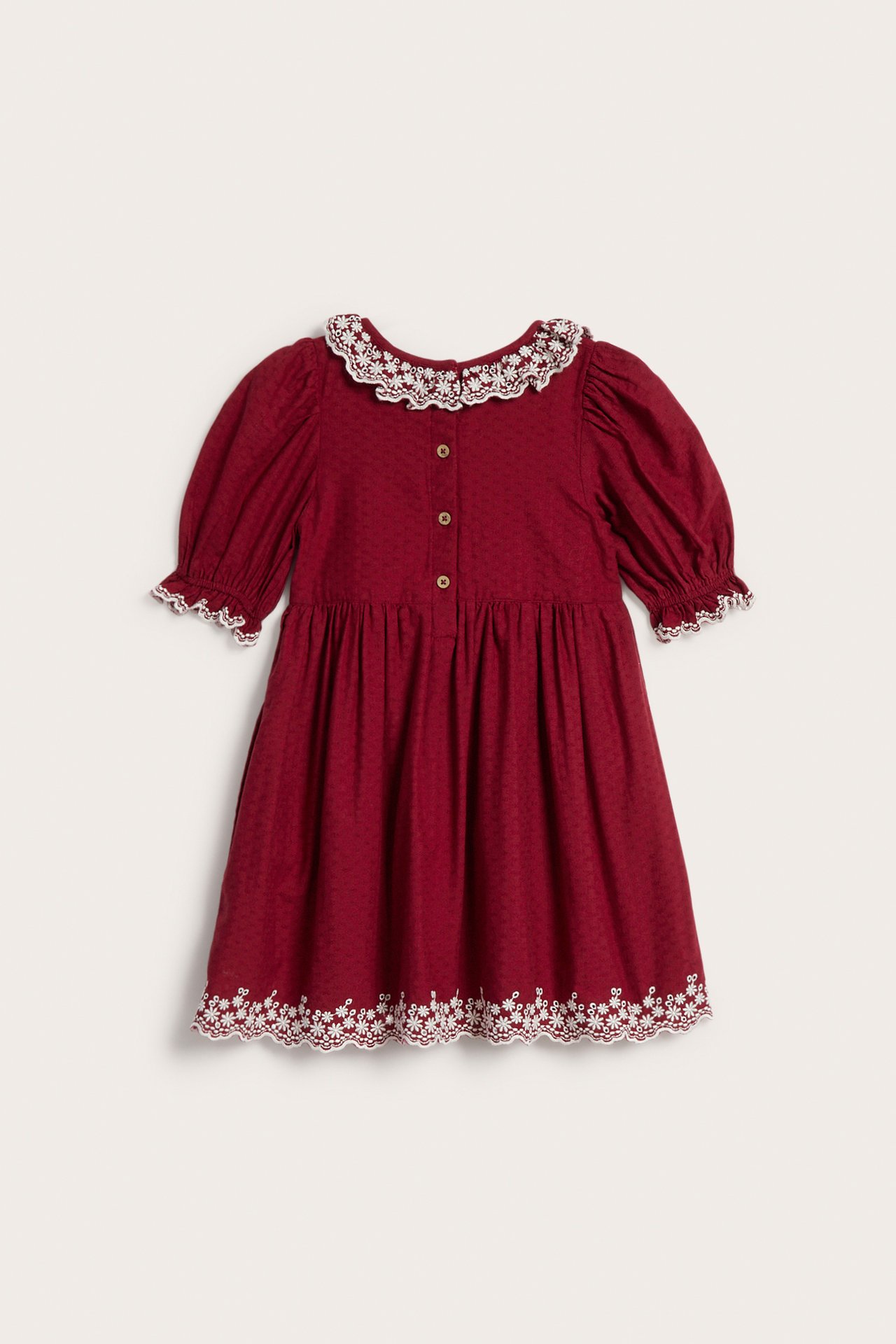 Frontbilde av en rød prikkete barnekjole med hvit blondekrage, mansjetter og brodert kant.