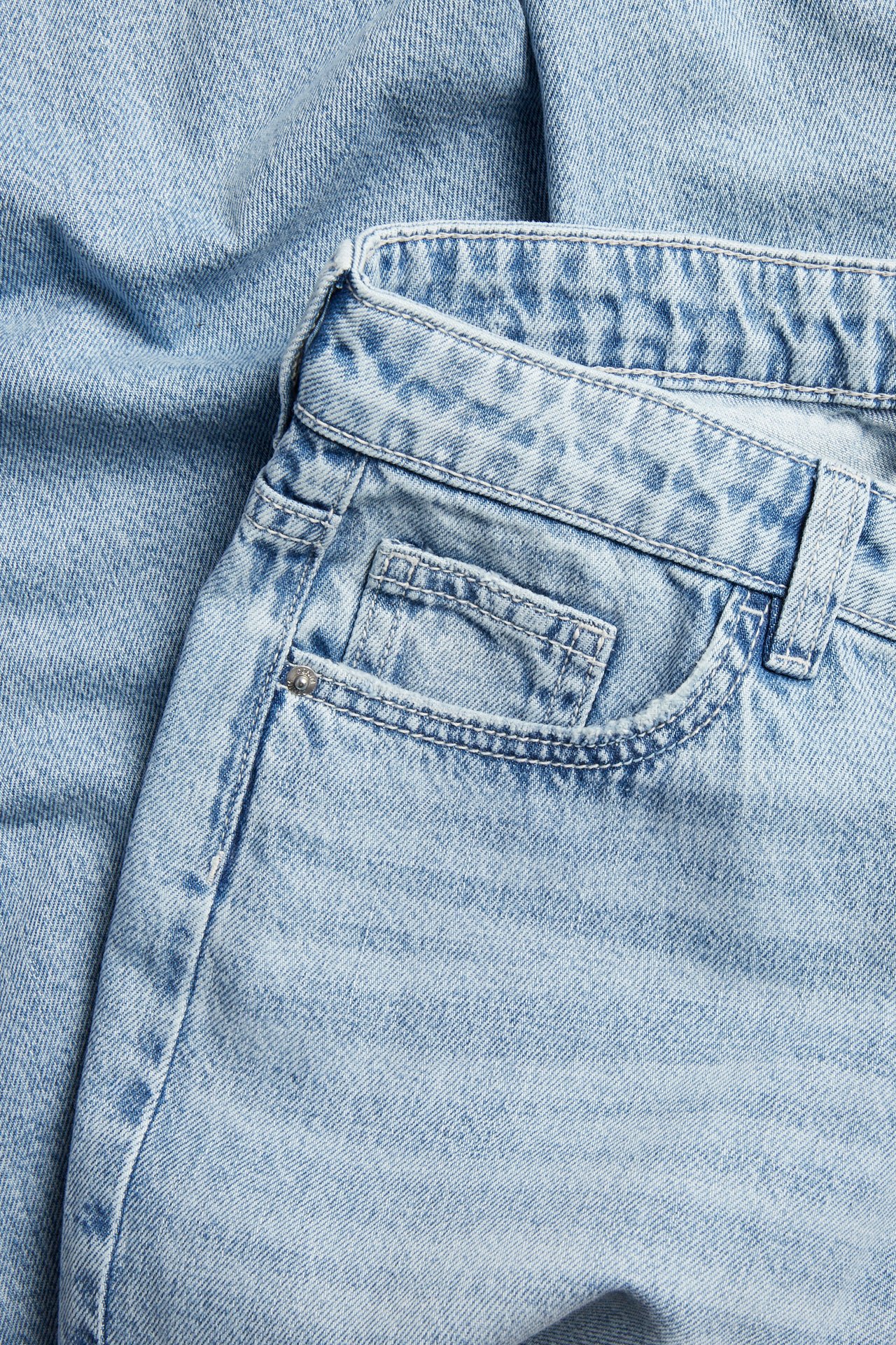 Närbild på ljusblå jeans i denim med framficka och nit.