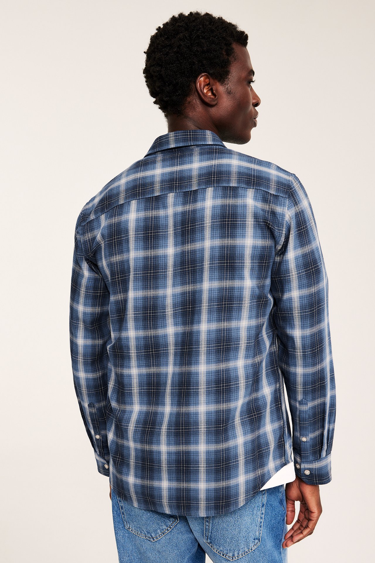 Bakfra av mannlig modell iført en blårutete langermet skjorte og blå jeans.