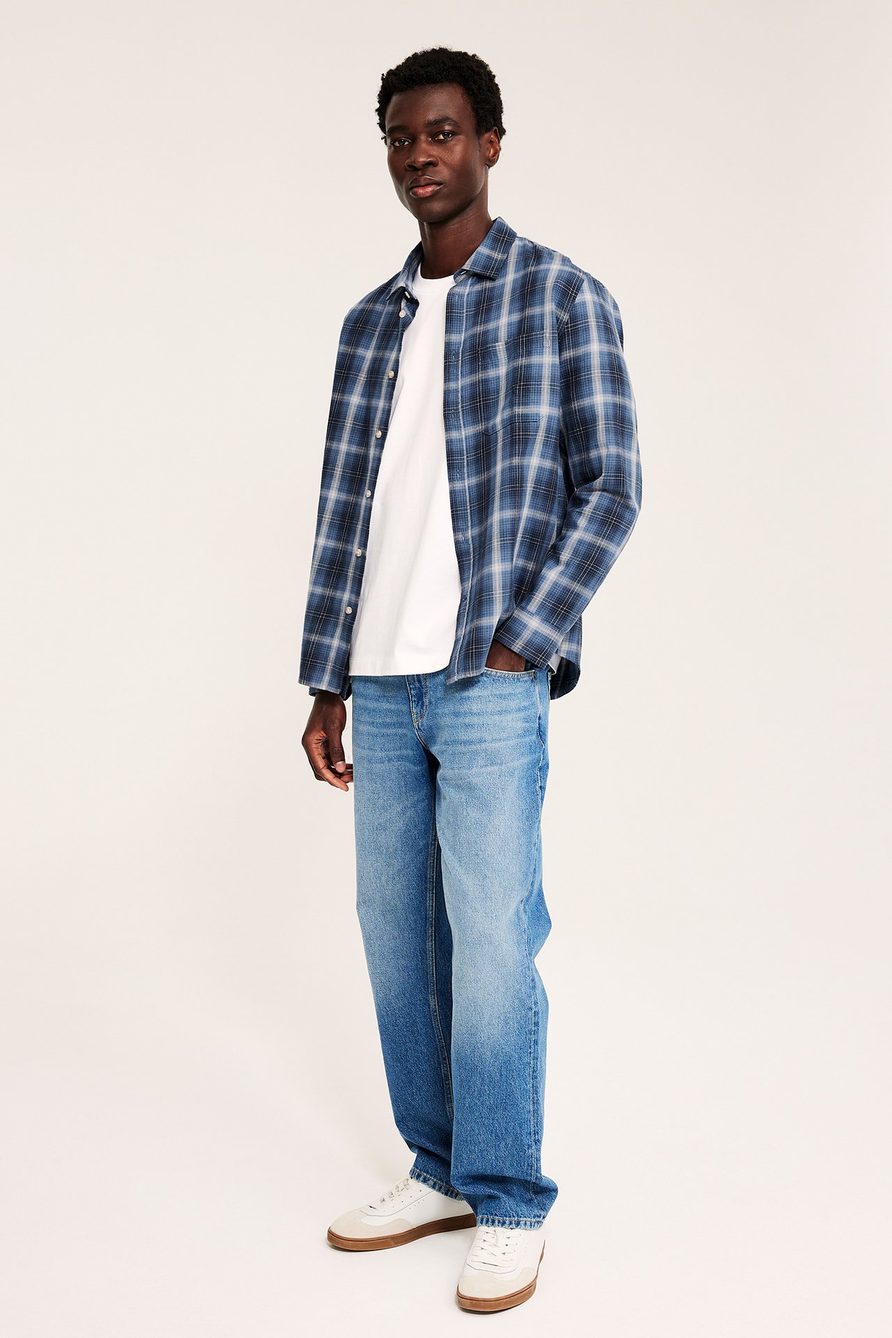Mann, forfra: blårutet langermet skjorte, hvit t-skjorte, blå jeans og hvite joggesko.