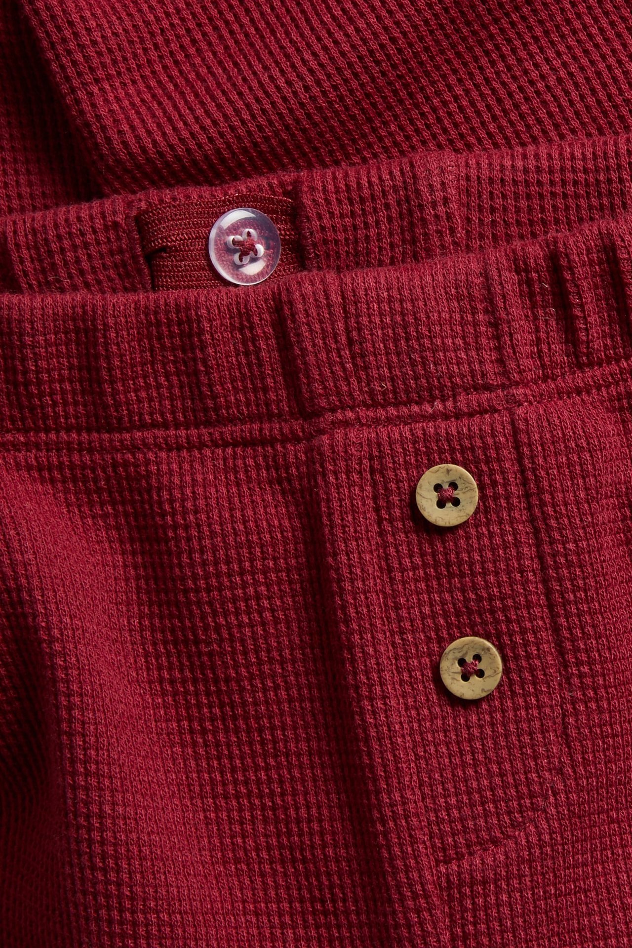 Nærbilde av et rødt ribbet pyjamasplagg med en gjennomsiktig knapp og to treknapper.