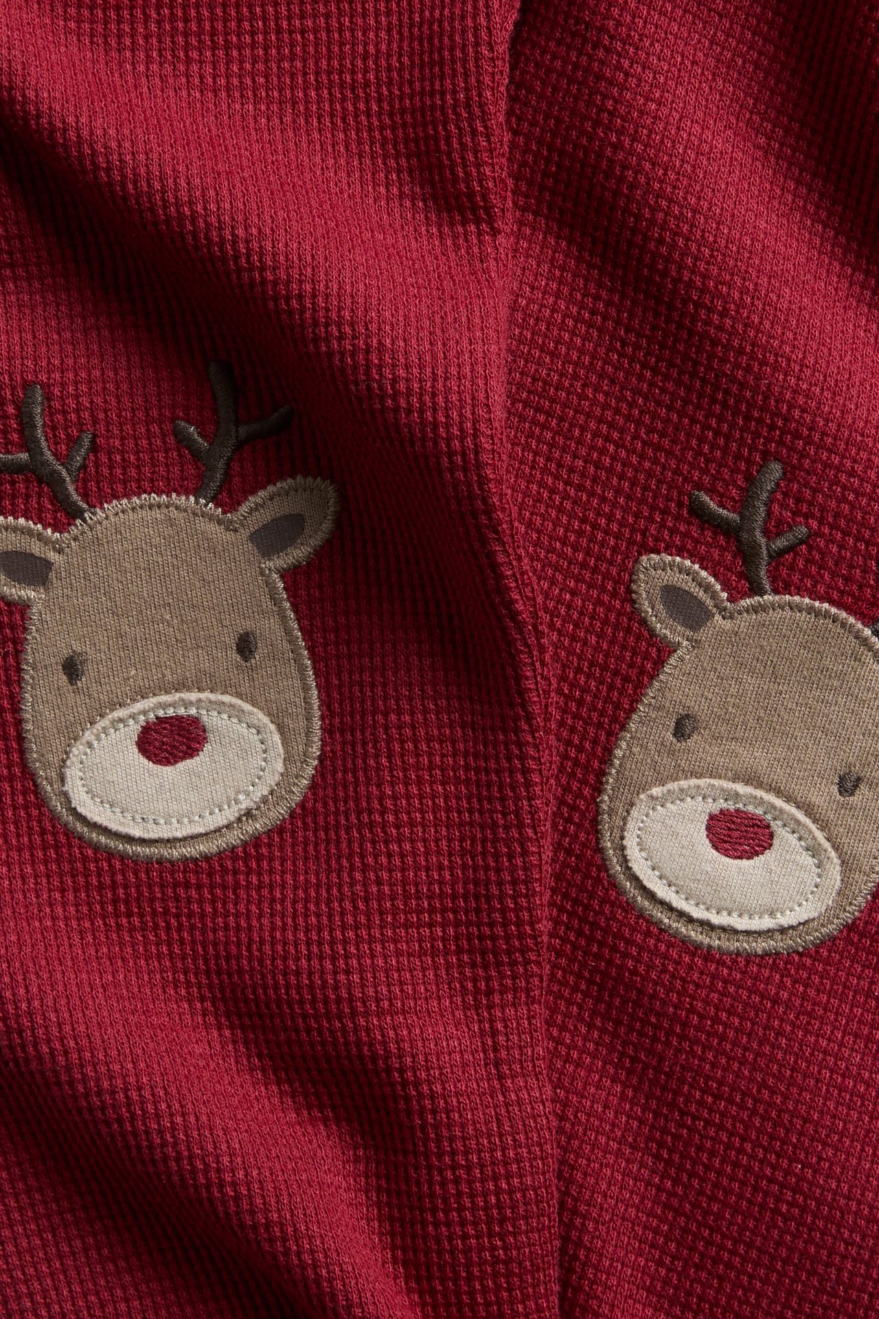Nærbilde av rødt ribbet stoff med to broderte brune reinsdyr-ansikter.