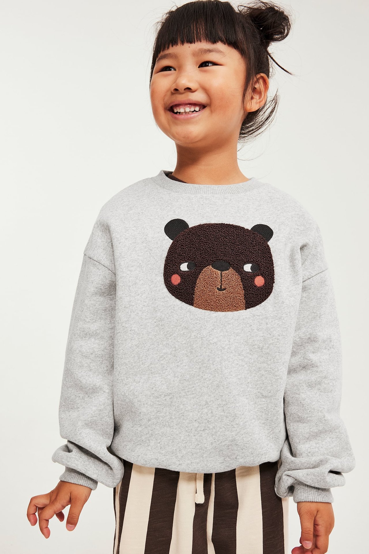 Frontbilde av et barn i grå sweatshirt med brodert bjørn og stripete bukser.