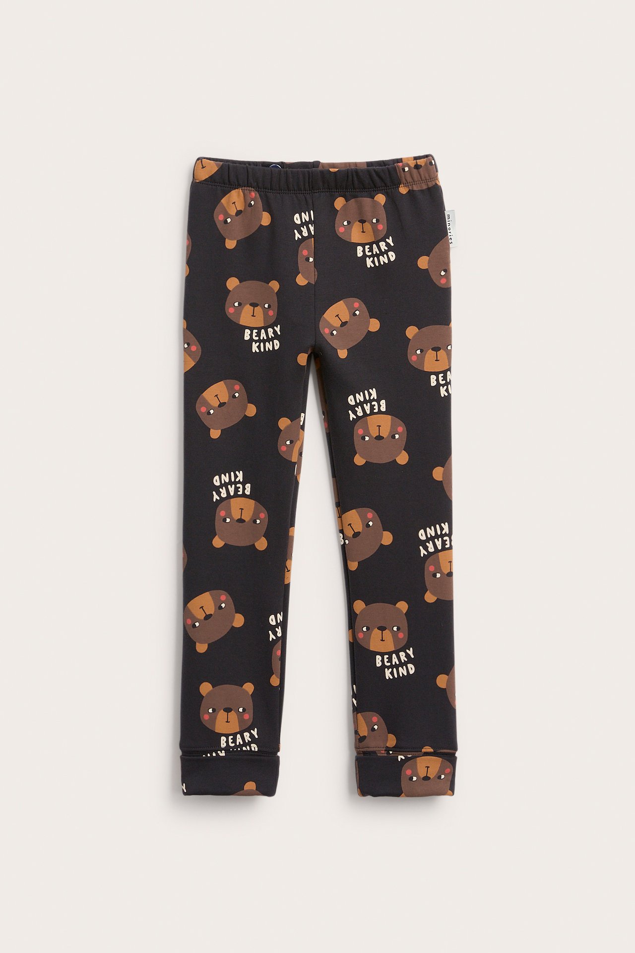 Edestä kuvattuna: Lasten mustat leggingsit kauttaaltaan ruskealla nalle- ja "BEARY KIND" -printillä.