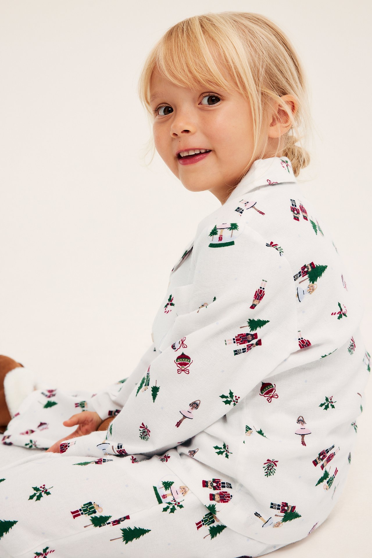 Hvit barnepyjamas med juletrykk, langermet topp og bukser, sett fra siden.