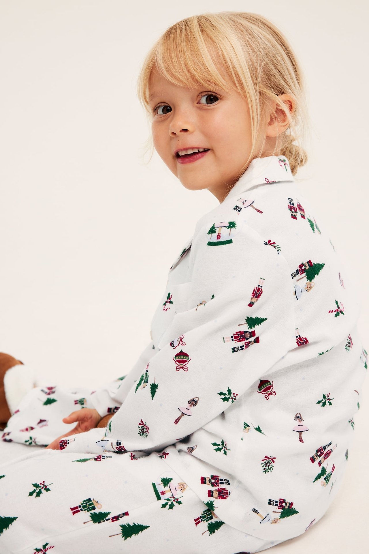 Hvit barnepyjamas med juletrykk, langermet topp og bukser, sett fra siden.