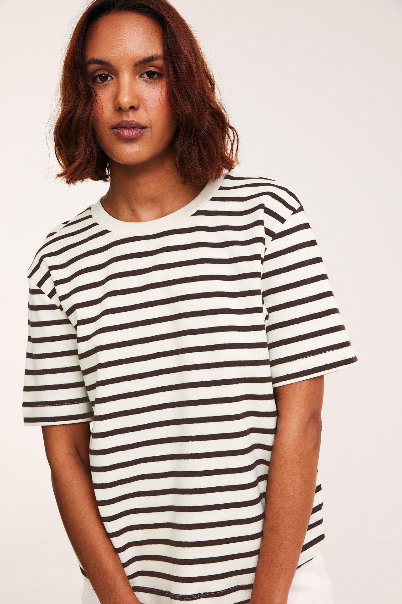 Framifrån: kvinna i en oversized, gräddvit och mörkbrun randig bomulls-t-shirt med vita byxor.