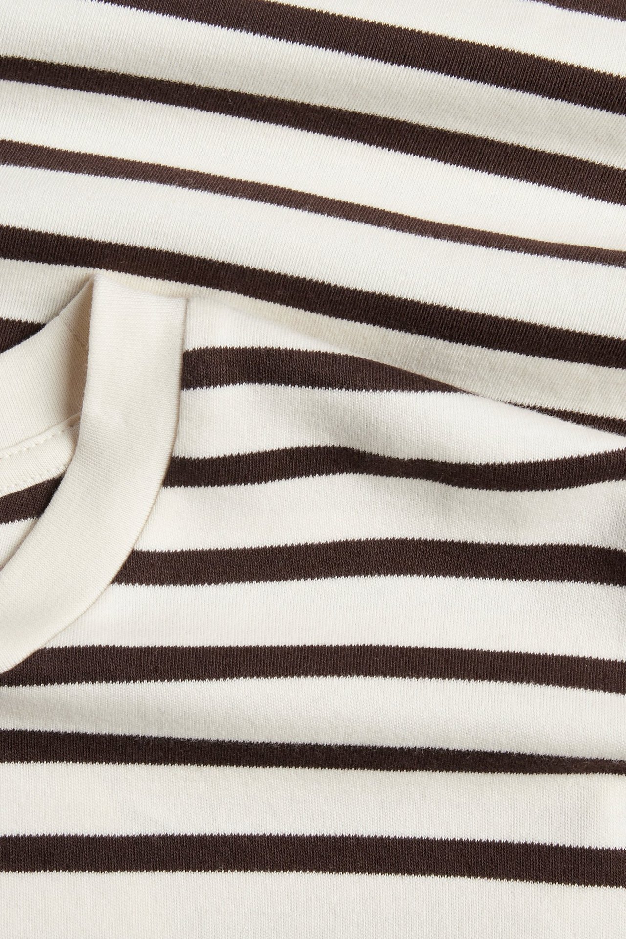 Zbliżenie na brązowo-białą, pasiastą, oversizową koszulkę bawełnianą z prążkowanym dekoltem.