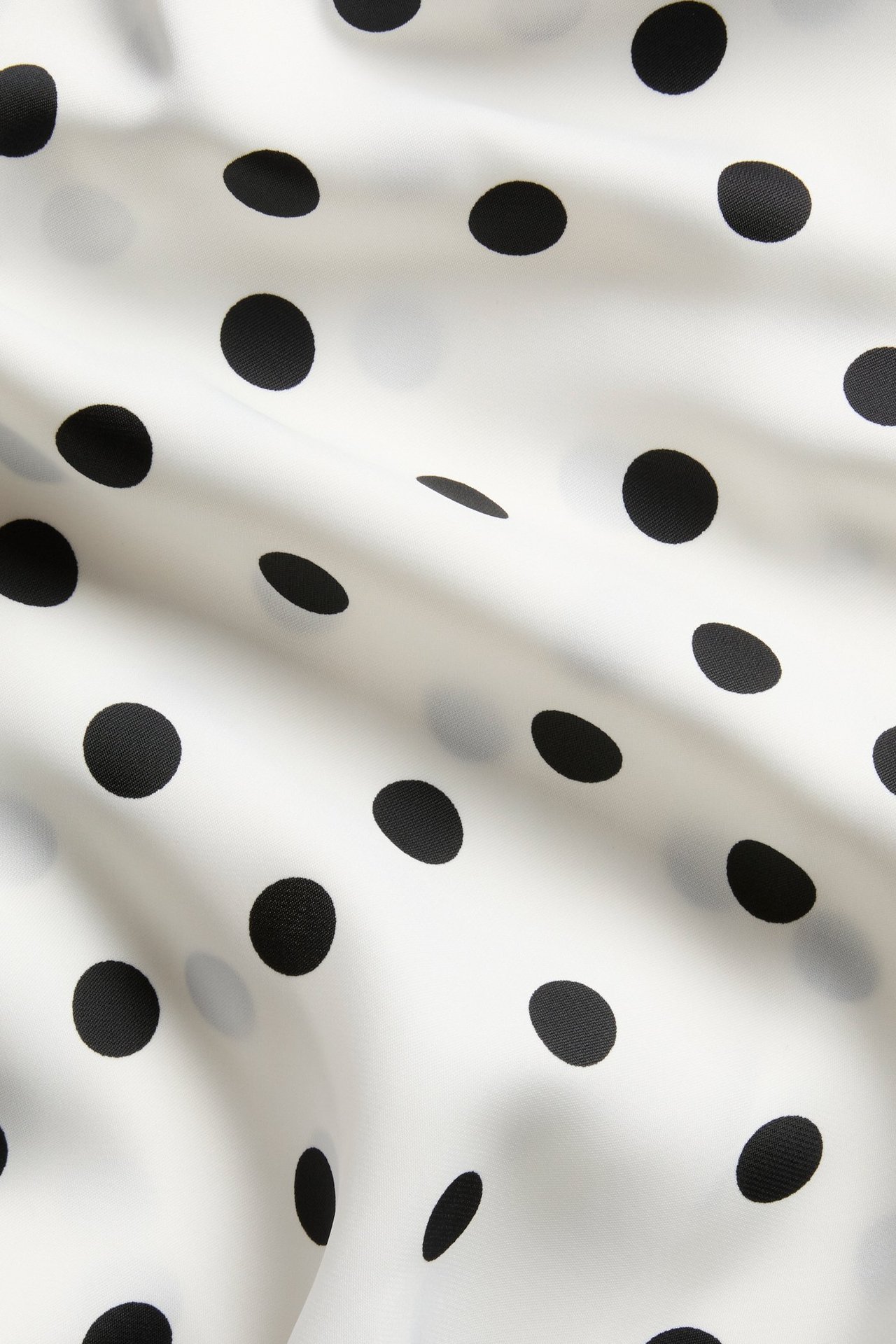 Nærbilde av offwhite satengstoff med svarte prikker og myke folder.