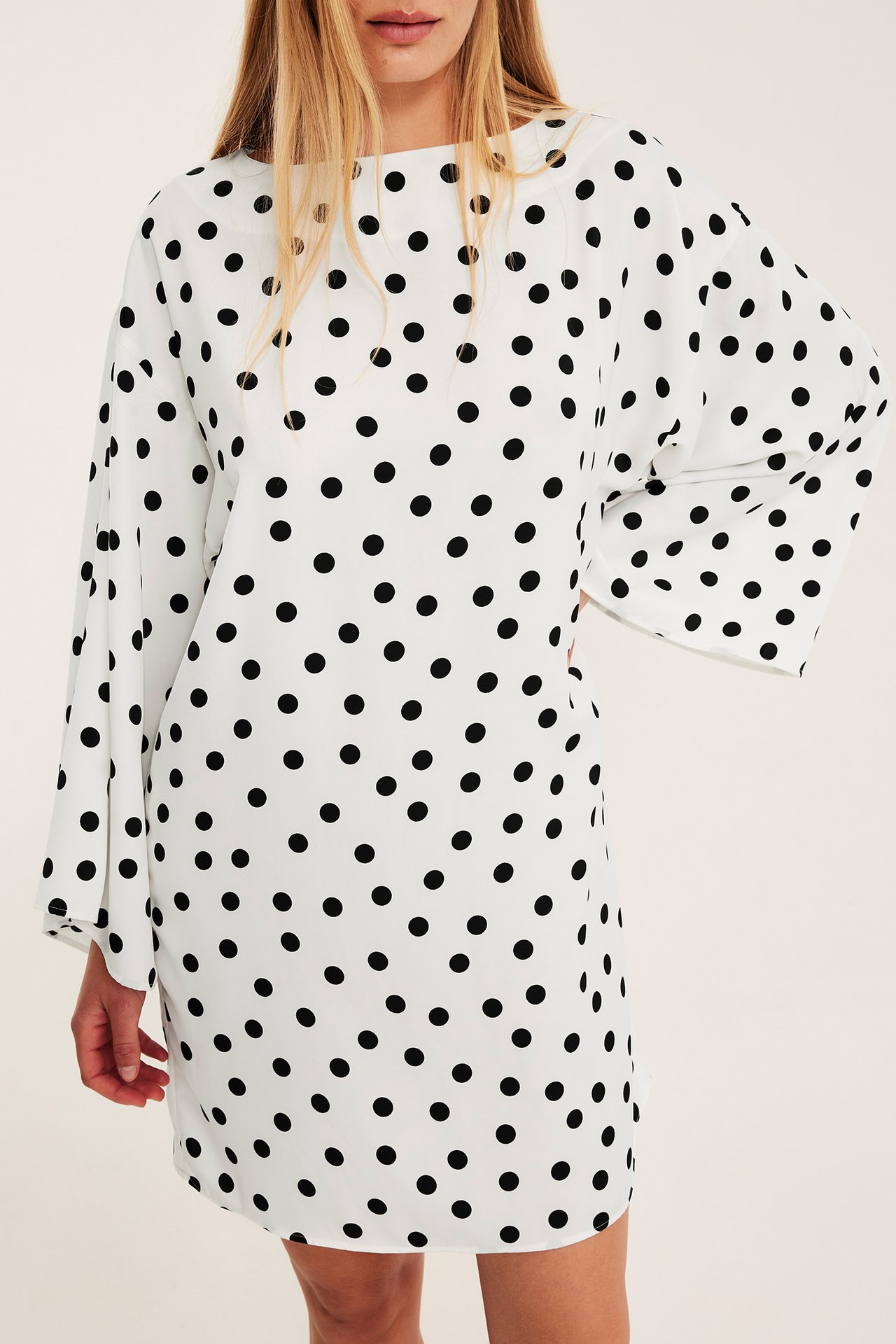 Edestä, nainen lyhyessä luonnonvalkoisessa pilkullisessa satiinimekossa, jossa leveät hihat.