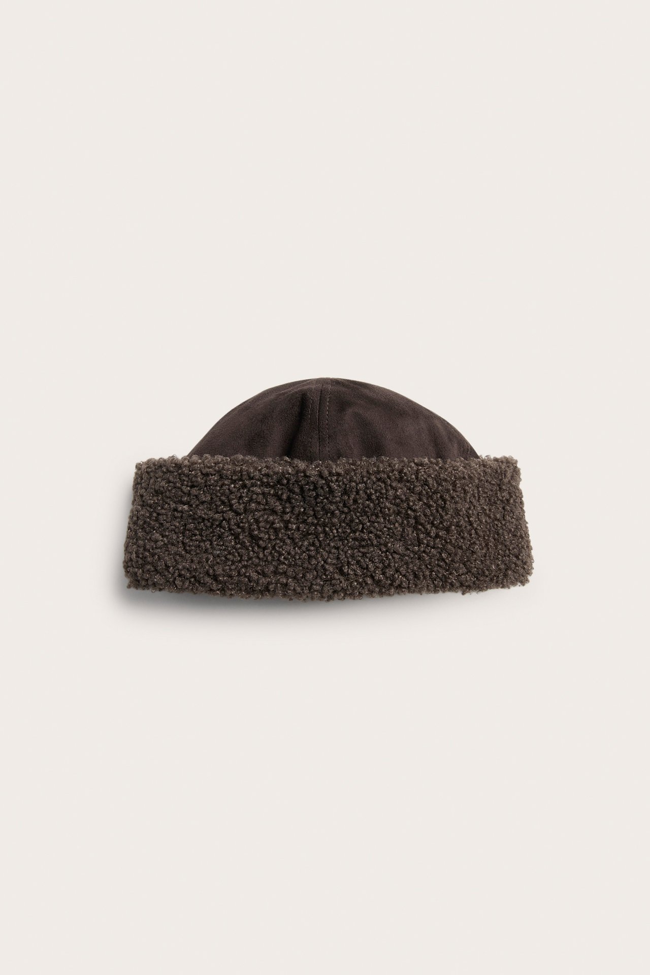 Frontal visning av en mørkebrun lue i semsket skinn med sherpakanter.