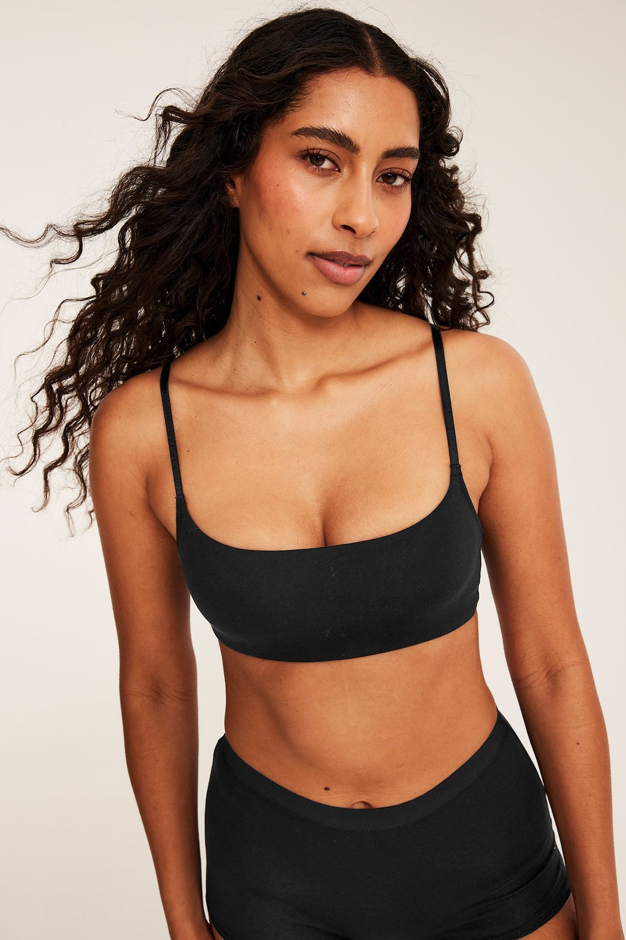 Framifrån, kvinnlig modell i svart bralette och svarta trosor.