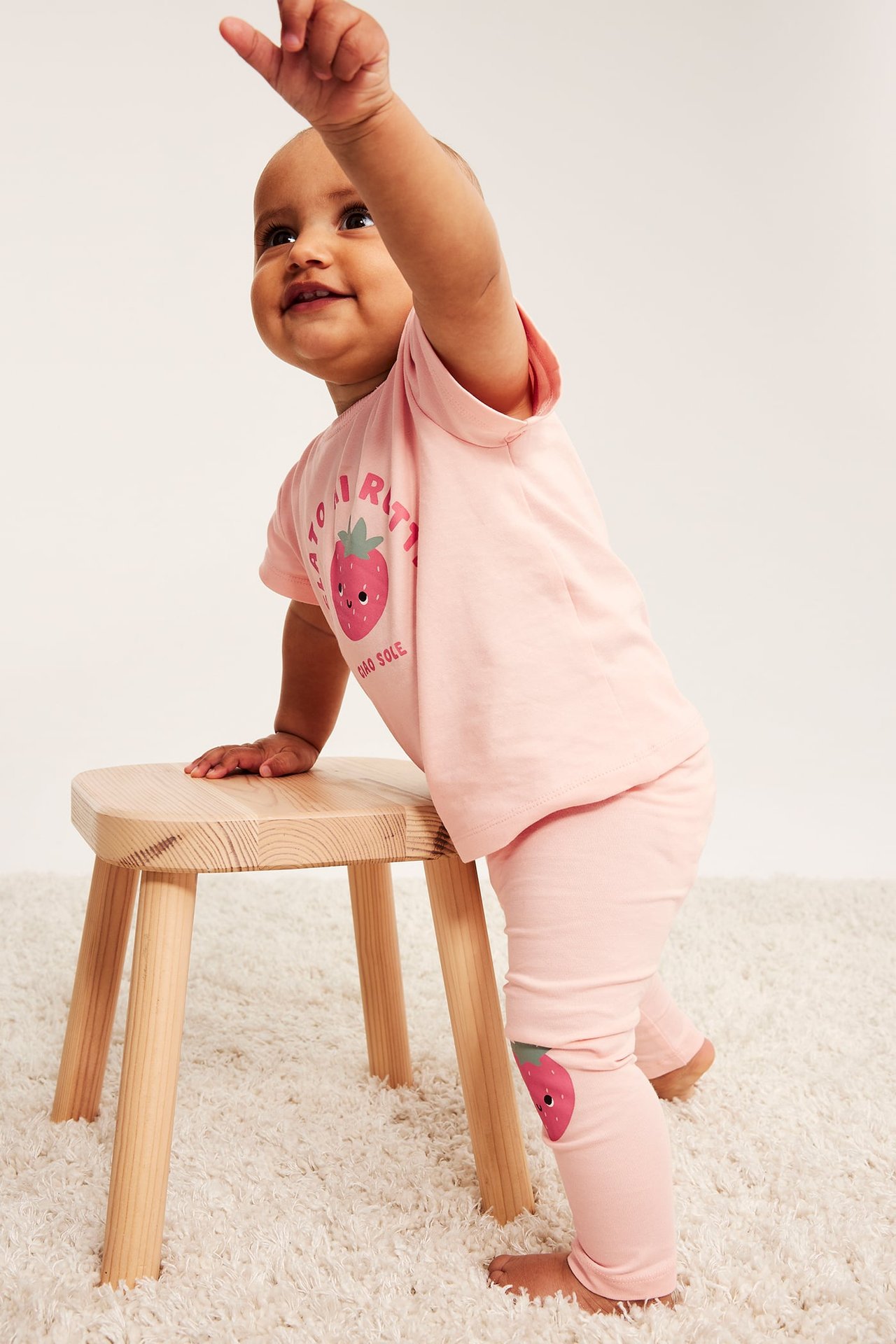 Widok z boku: niemowlę w jasnoróżowym T-shircie z truskawką i pasujących legginsach.