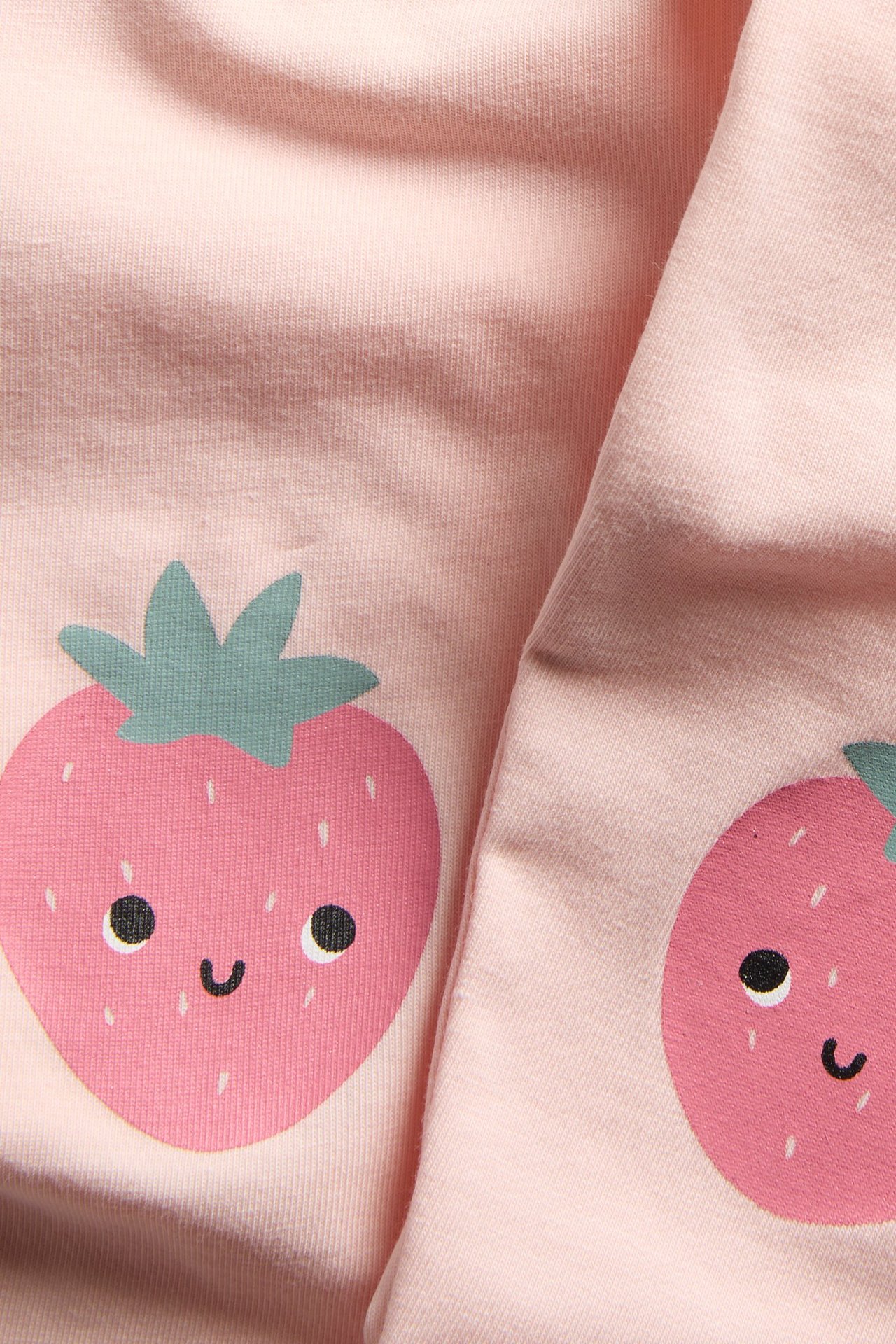 Zbliżenie jasnoróżowych legginsów dziecięcych z uroczą aplikacją truskawki na kolanie.