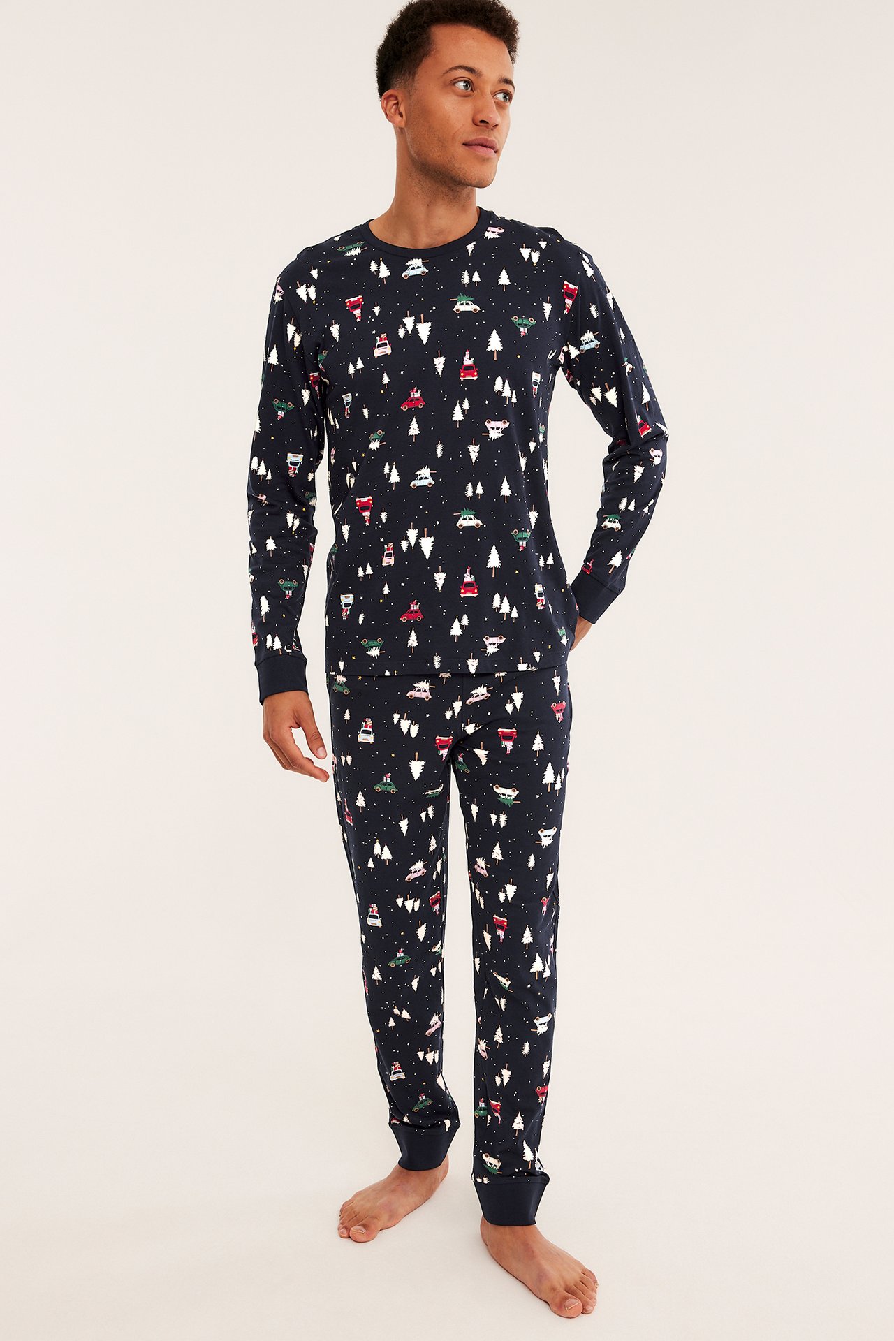 Framsida av en man i marinblå pyjamas med tryck av vita julgranar och fordon.