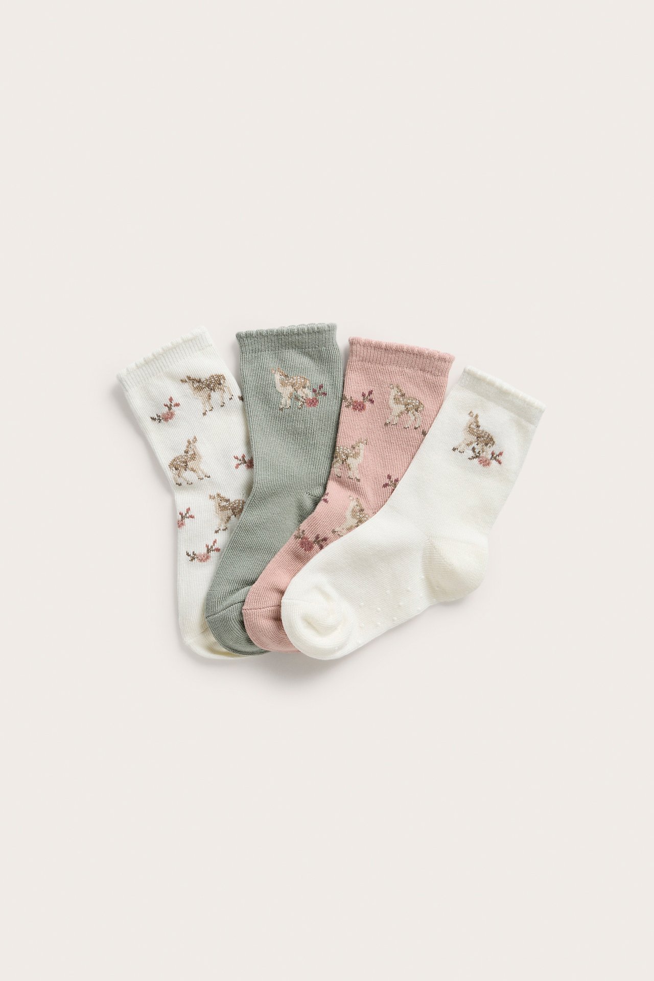 Ovanifrån: Fyra par mönstrade barnstrumpor i offwhite, salviagrön och rosa med rådjur och blommor.