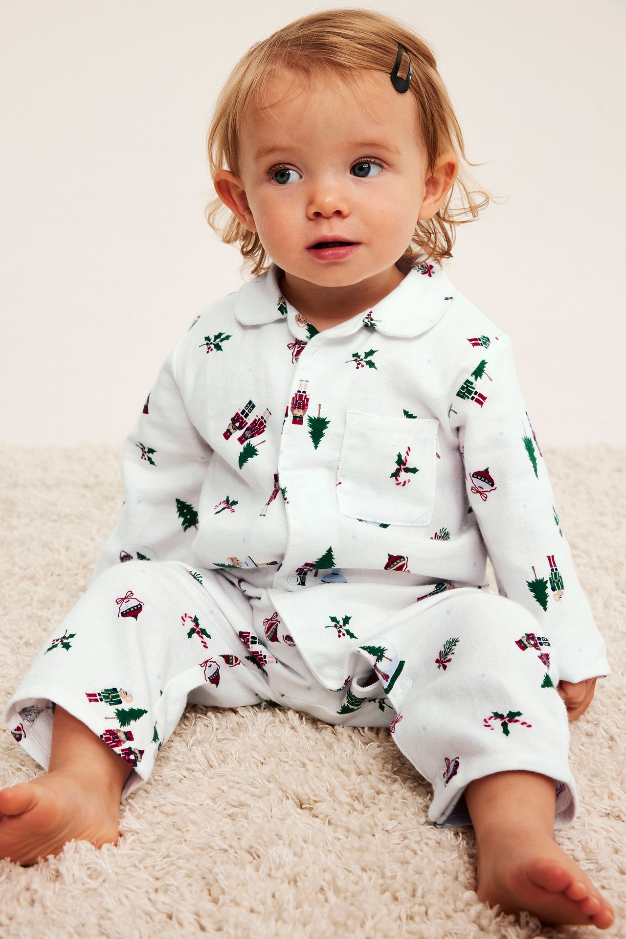 Framifrån, en bebis bär vit julmönstrad pyjamas med krage.