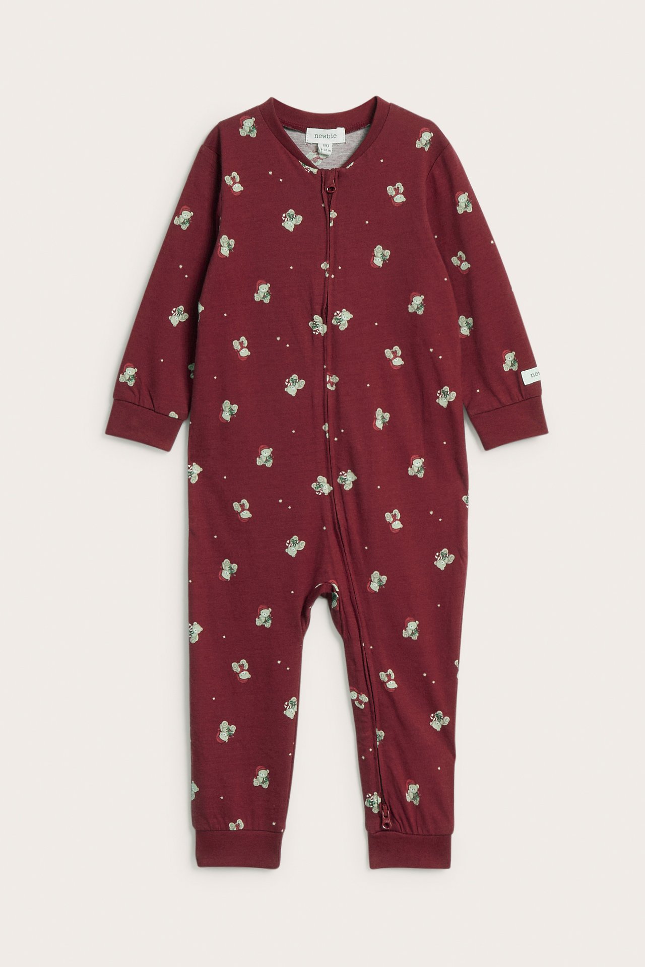 Framifrån en bebis mörkröd pyjamas med heltäckande nallebjörnsmönster och hellång dragkedja fram.