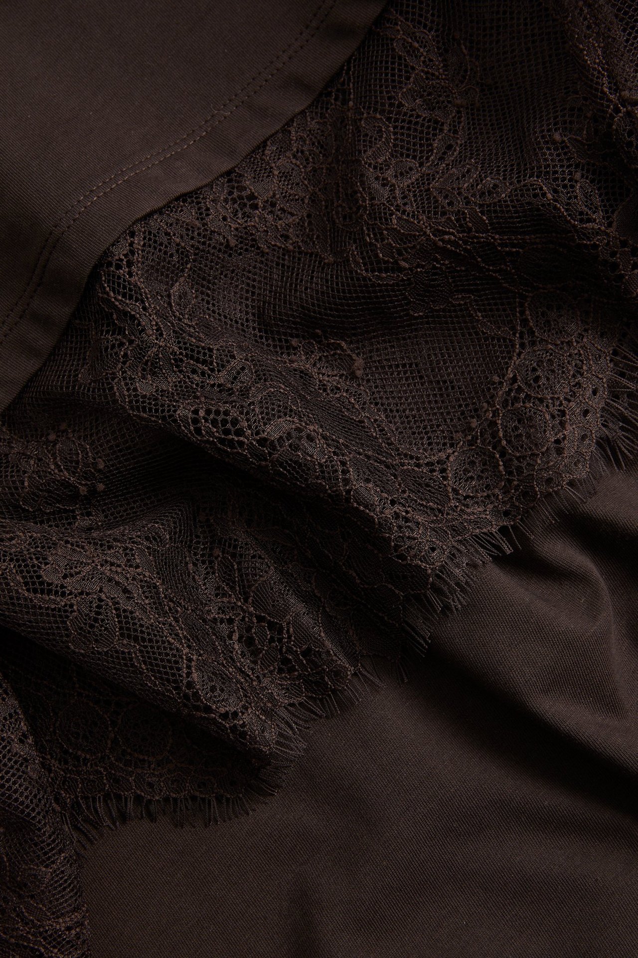 Nærbilde av en mørkbrun t-skjorte med intrikate blonder i nederkanten.