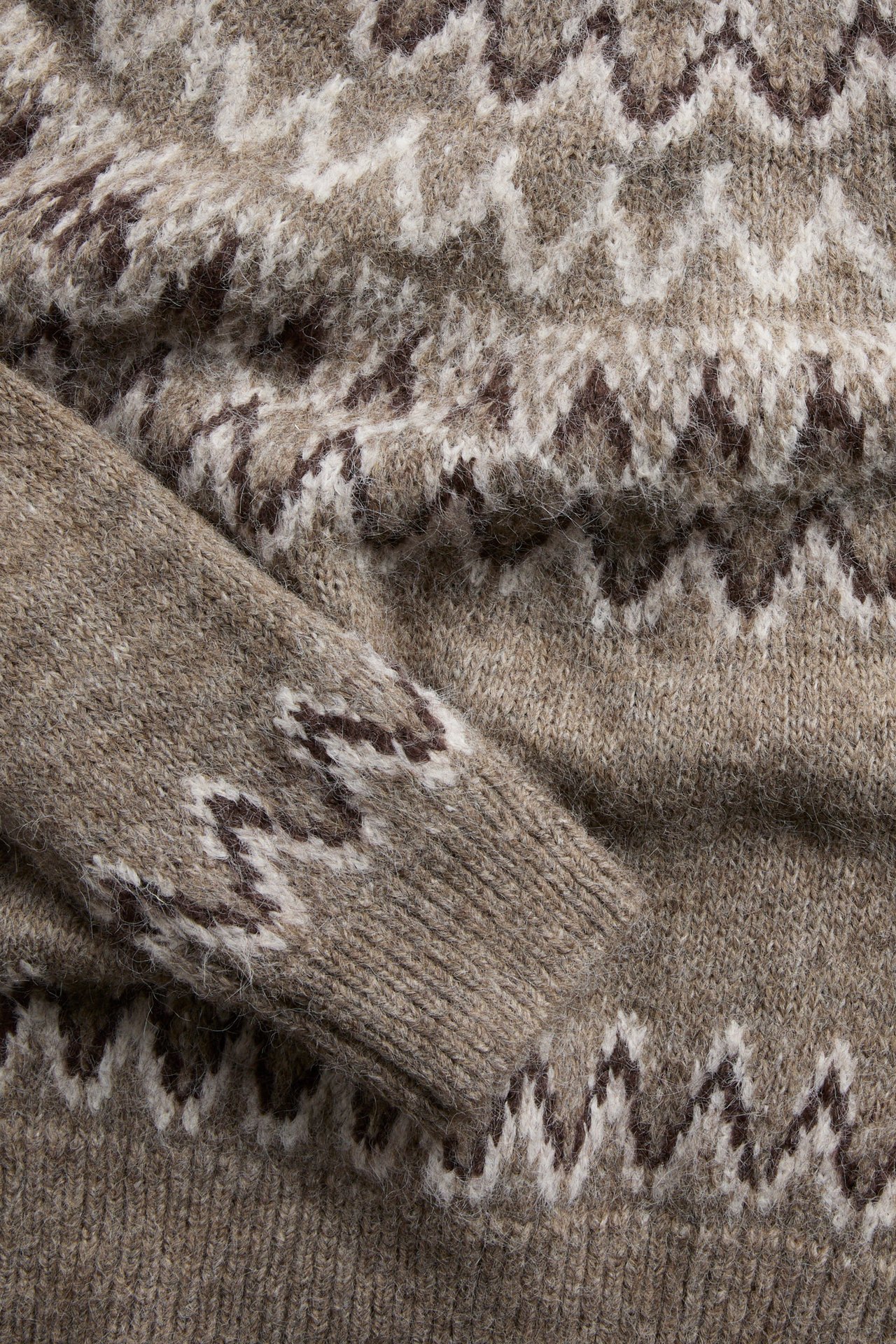 Nærbilde av en beige Fair Isle strikket genser med brune og hvitmønstrede detaljer.